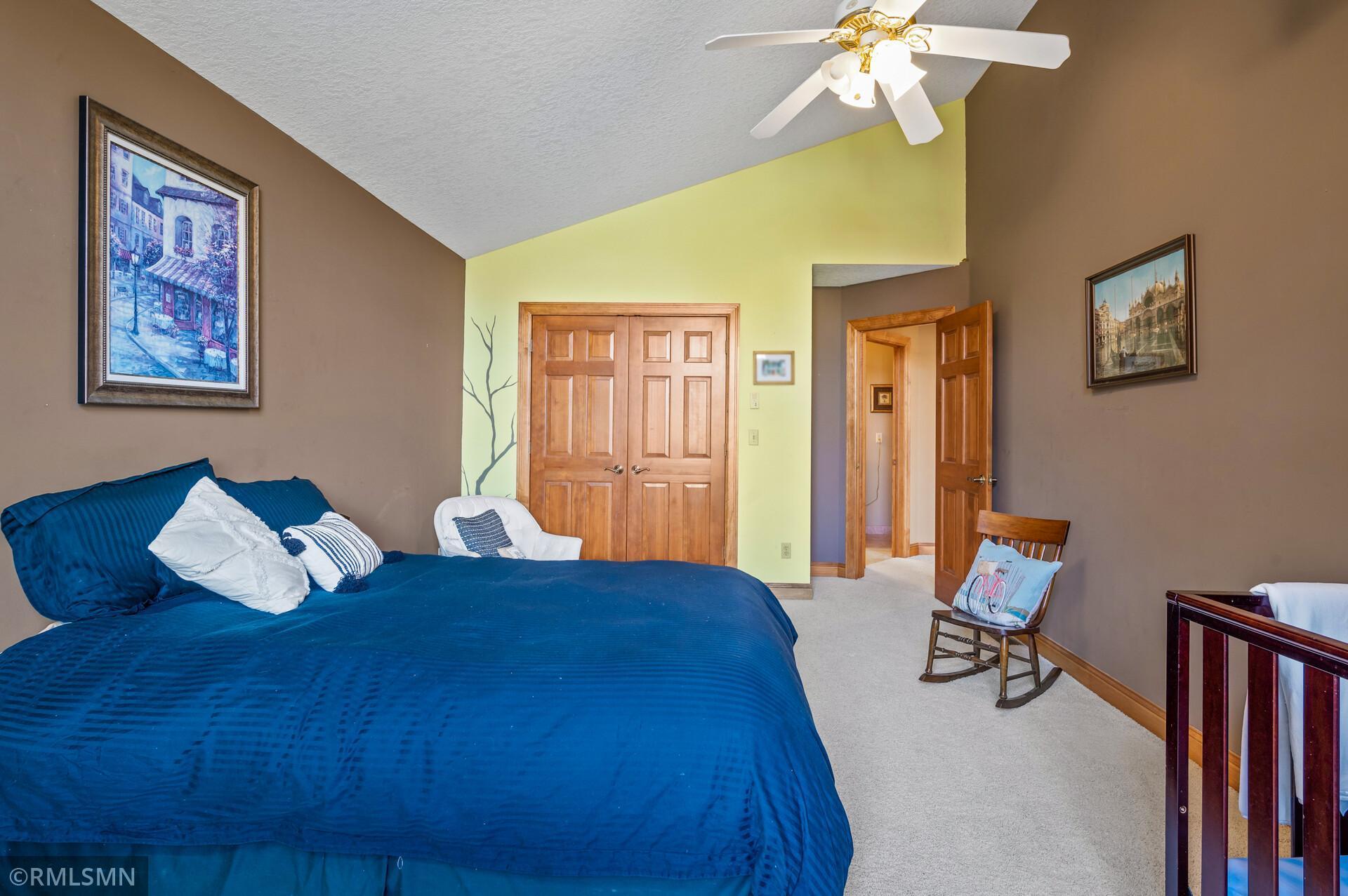 Bedroom with a large blue bed, wooden double doors, and a white ceiling fan.