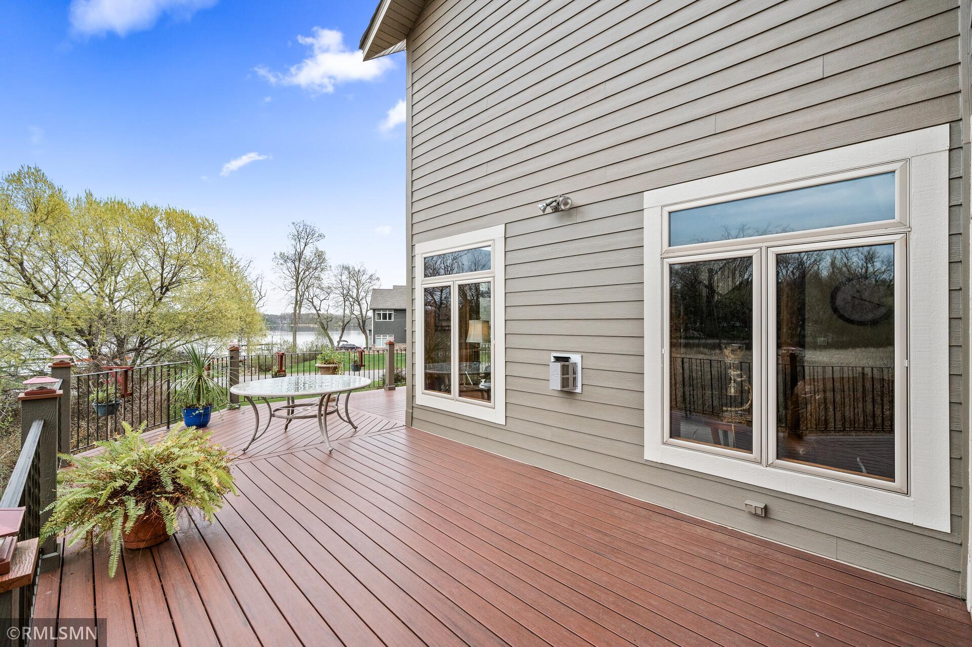 Wooden deck beside a gray-sided home, with patio furniture, potted plants, and a lake view.