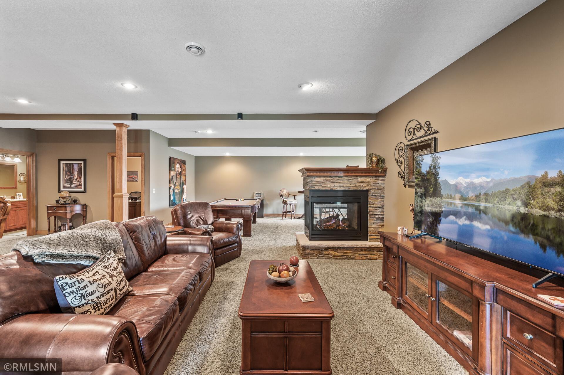 Basement family room with leather seating, a stone fireplace, television, and pool table.