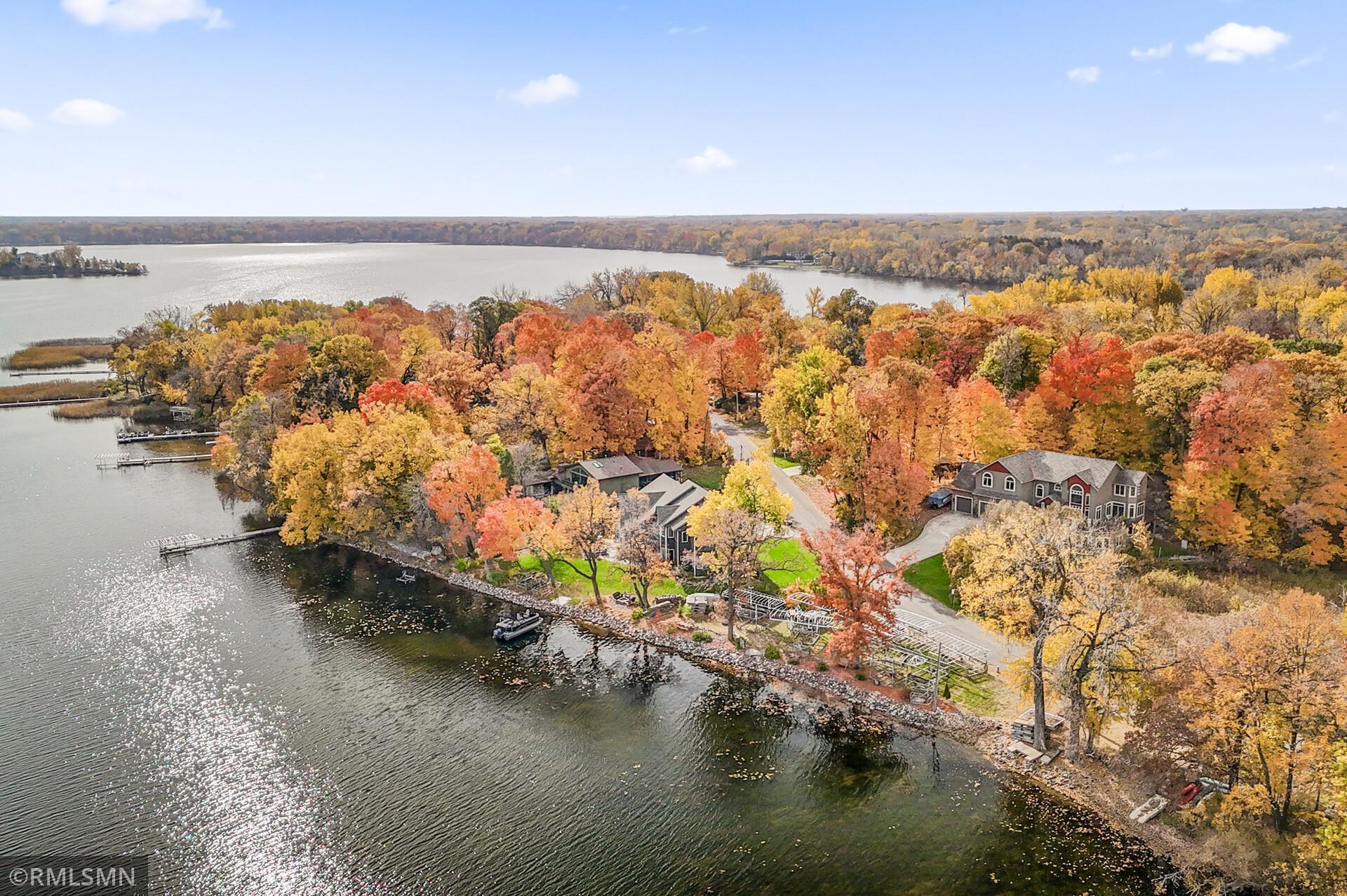 Aerial view of lakefront homes and docks surrounded by vivid autumn foliage.