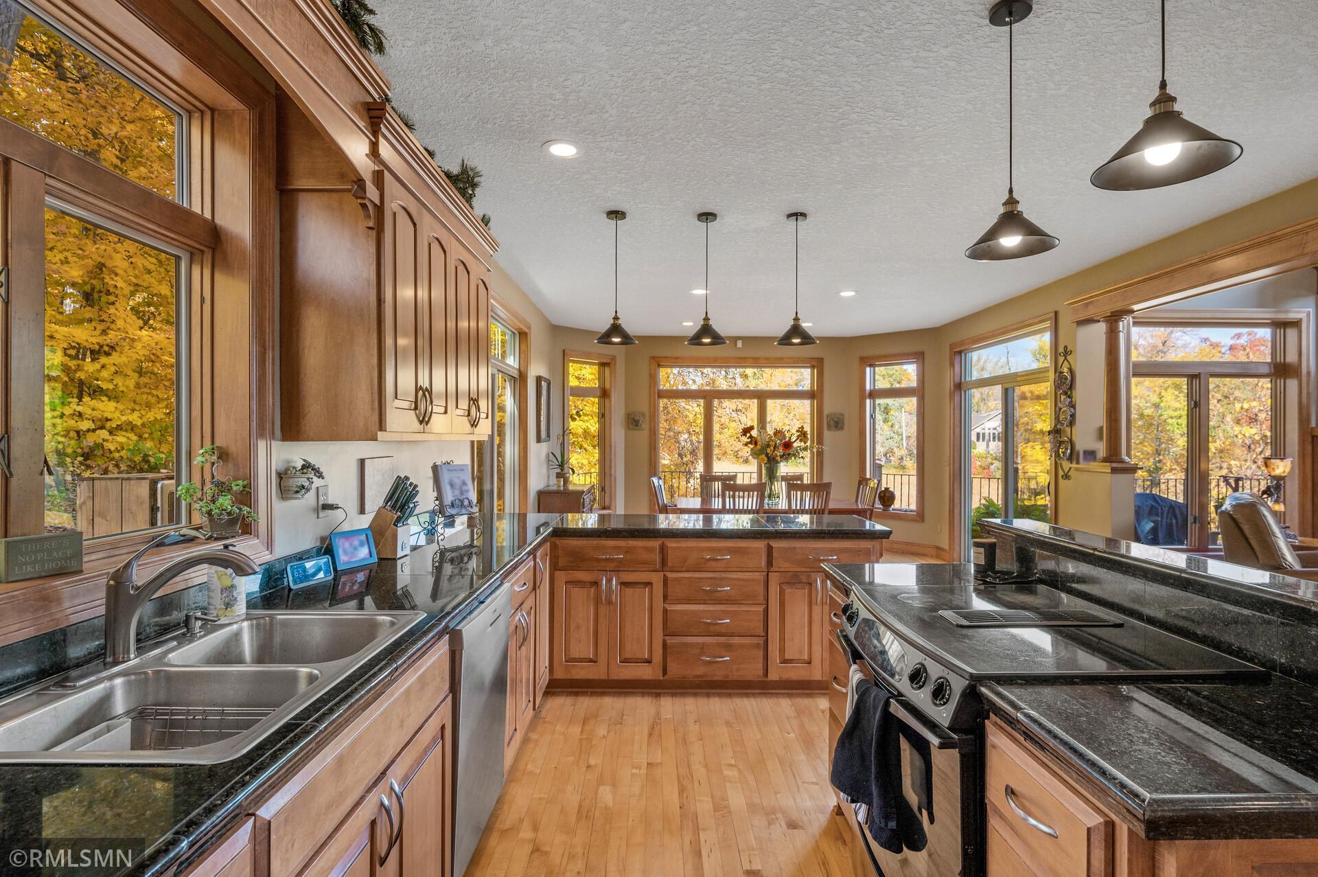 Kitchen with wood cabinetry, granite counters, stainless steel appliances, and large windows overlooking autumn trees.
