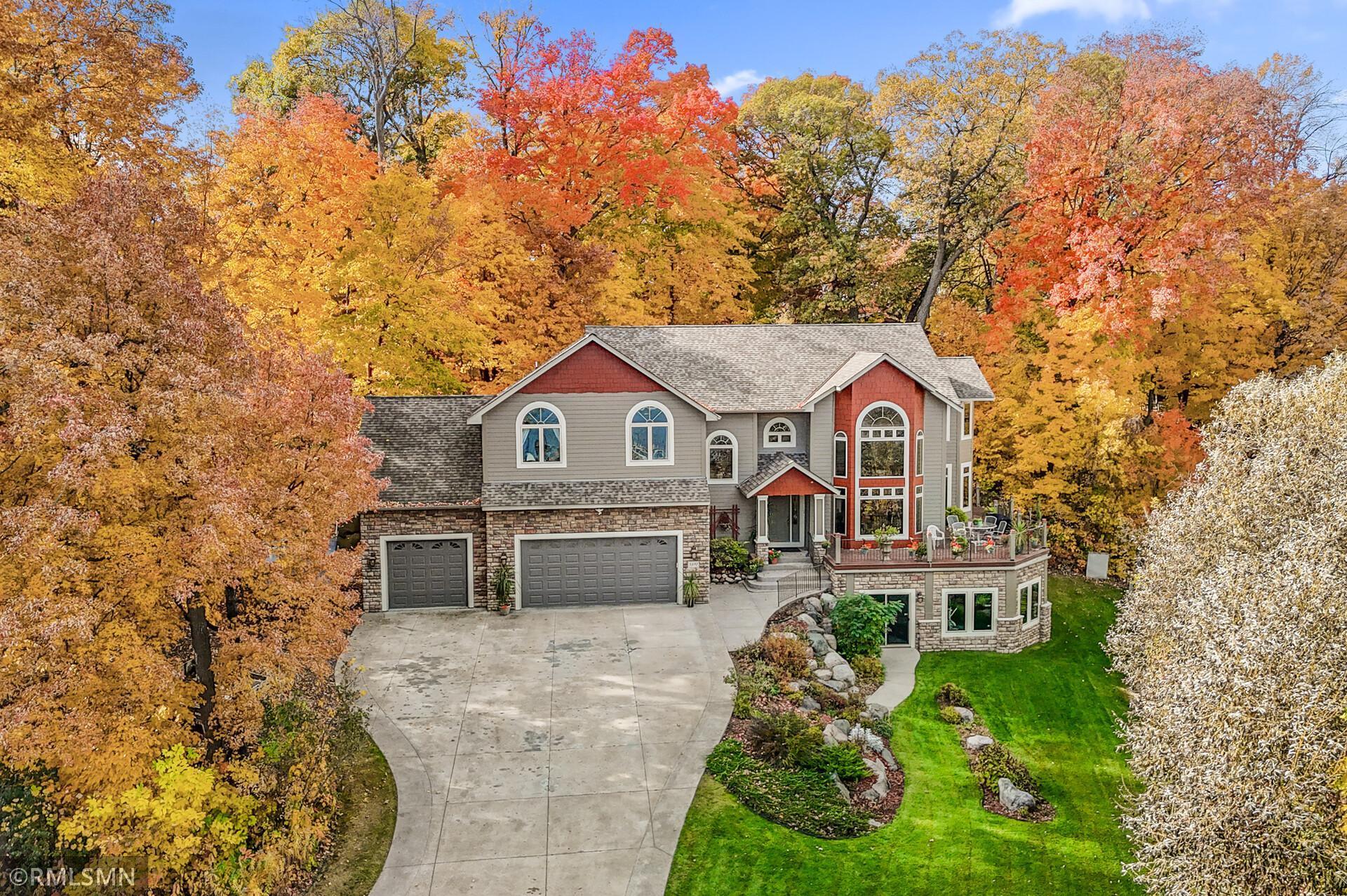 Two-story gray and red house with stone facade, curved driveway, and colorful autumn trees.