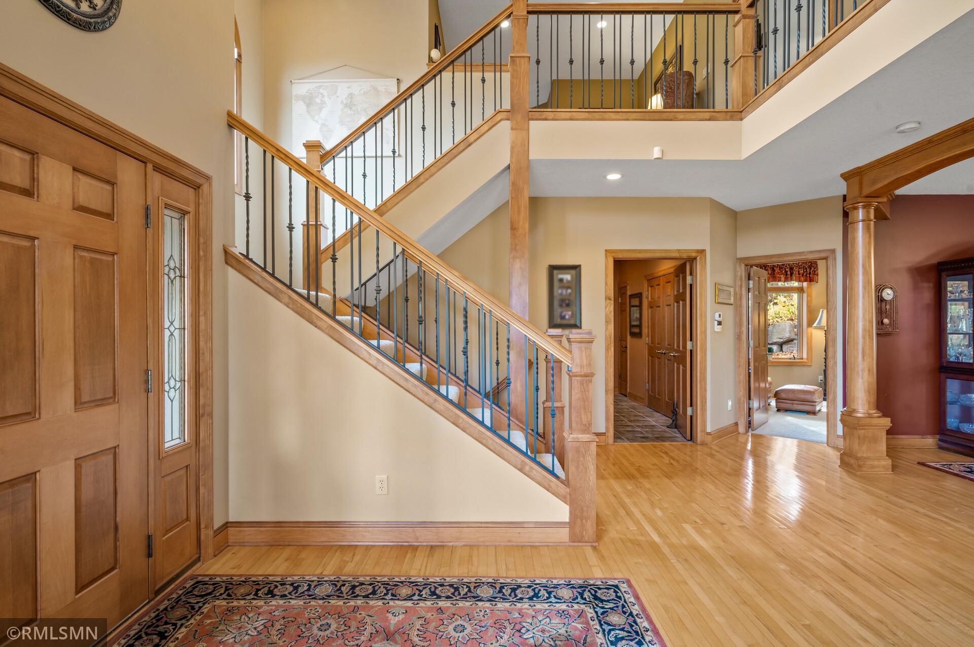 Foyer with a sweeping wood staircase, iron balusters, hardwood floors, and a paneled entry door.