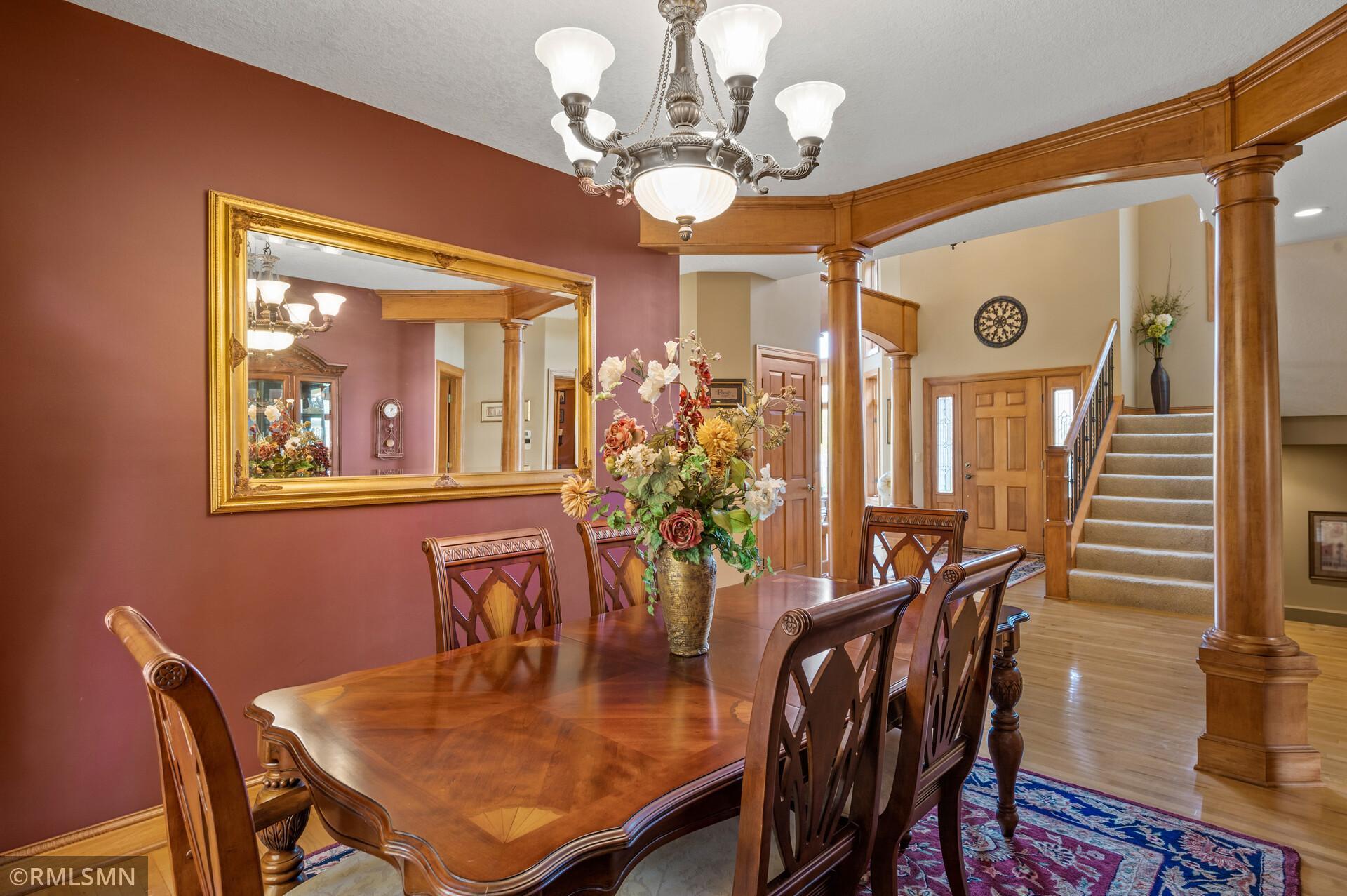 Furnished dining room with a polished wood table, burgundy walls, and a wood-trimmed archway to the staircase.