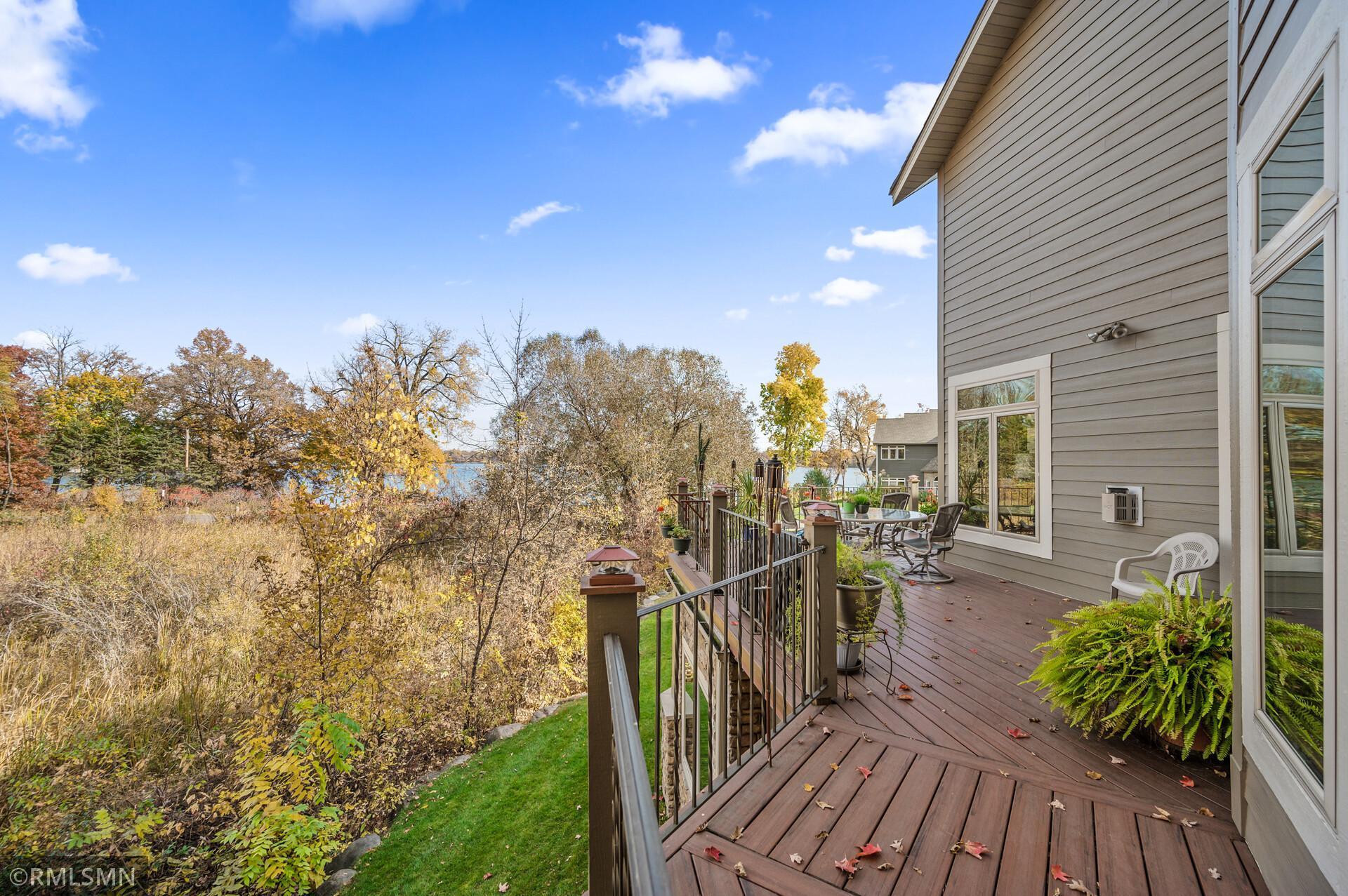 Wooden deck beside a gray home, with autumn trees and a glimpse of water beyond the railing.