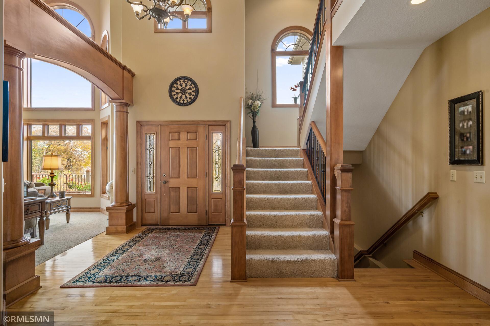 Two-story foyer with a carpeted staircase, arched windows, and a wood entry door.