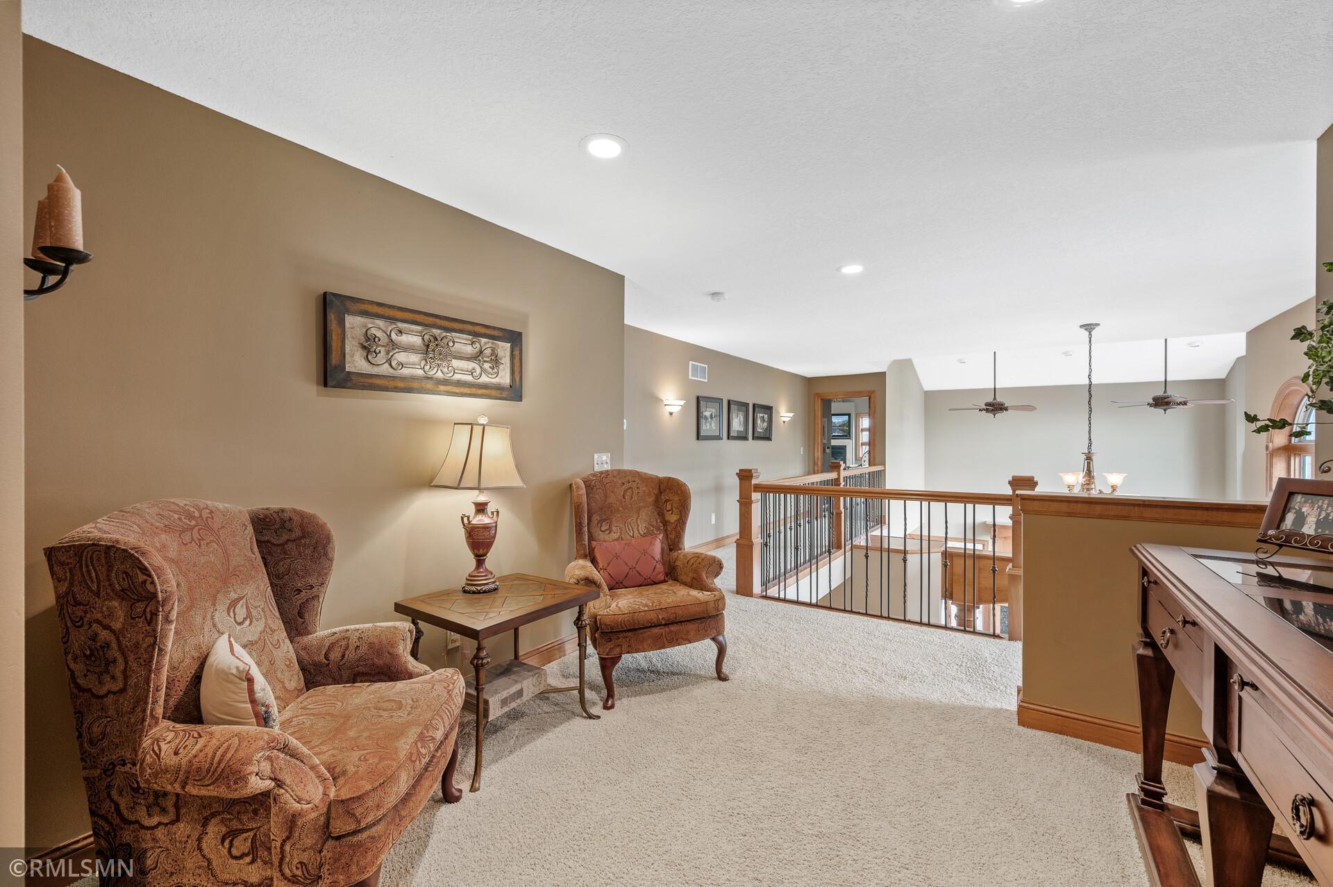 Upstairs sitting area with patterned armchairs beside a carpeted landing and wood-and-iron railing.