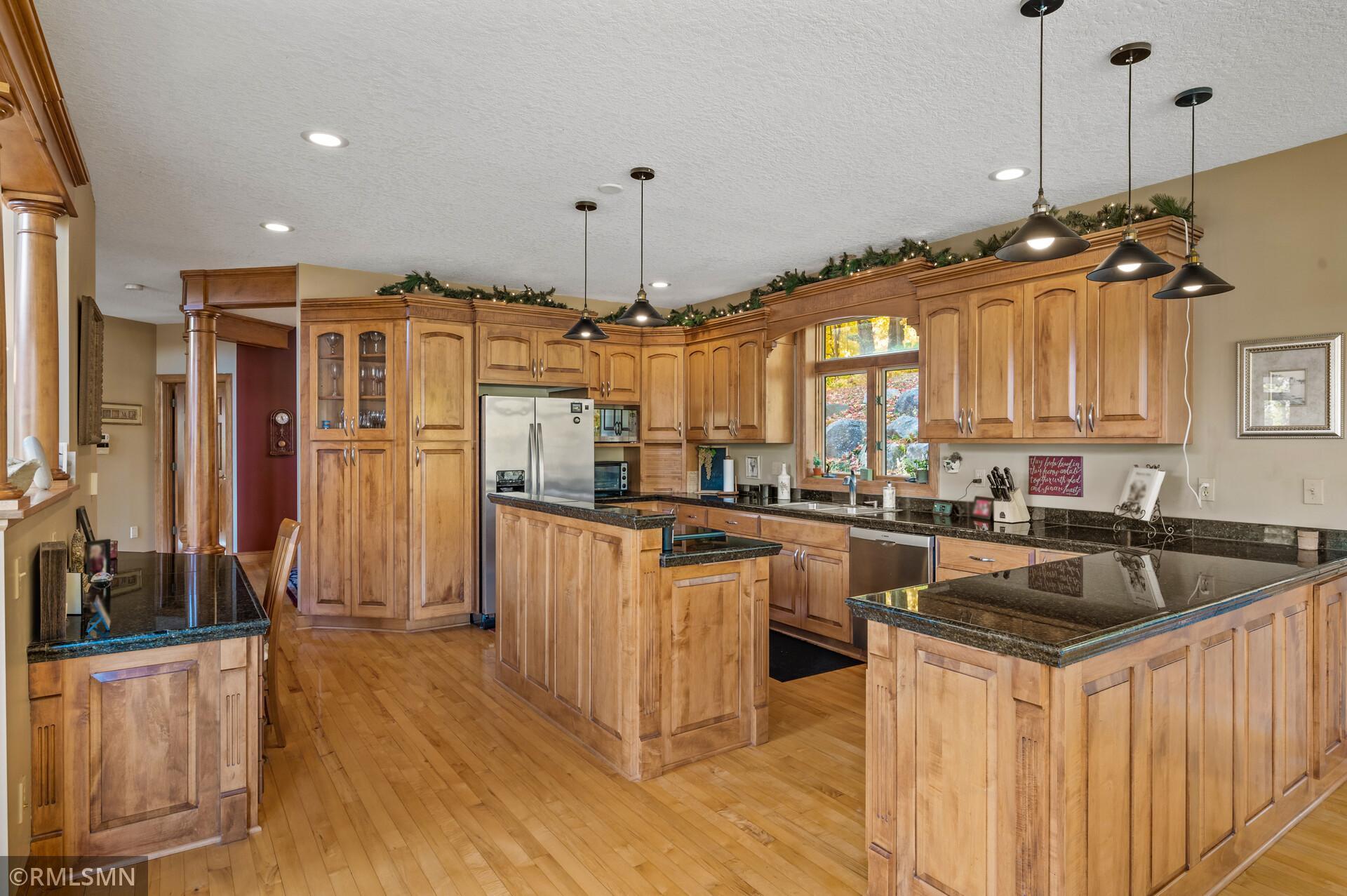 Kitchen with extensive honey-colored cabinetry, dark granite counters, multiple islands, and a large window.