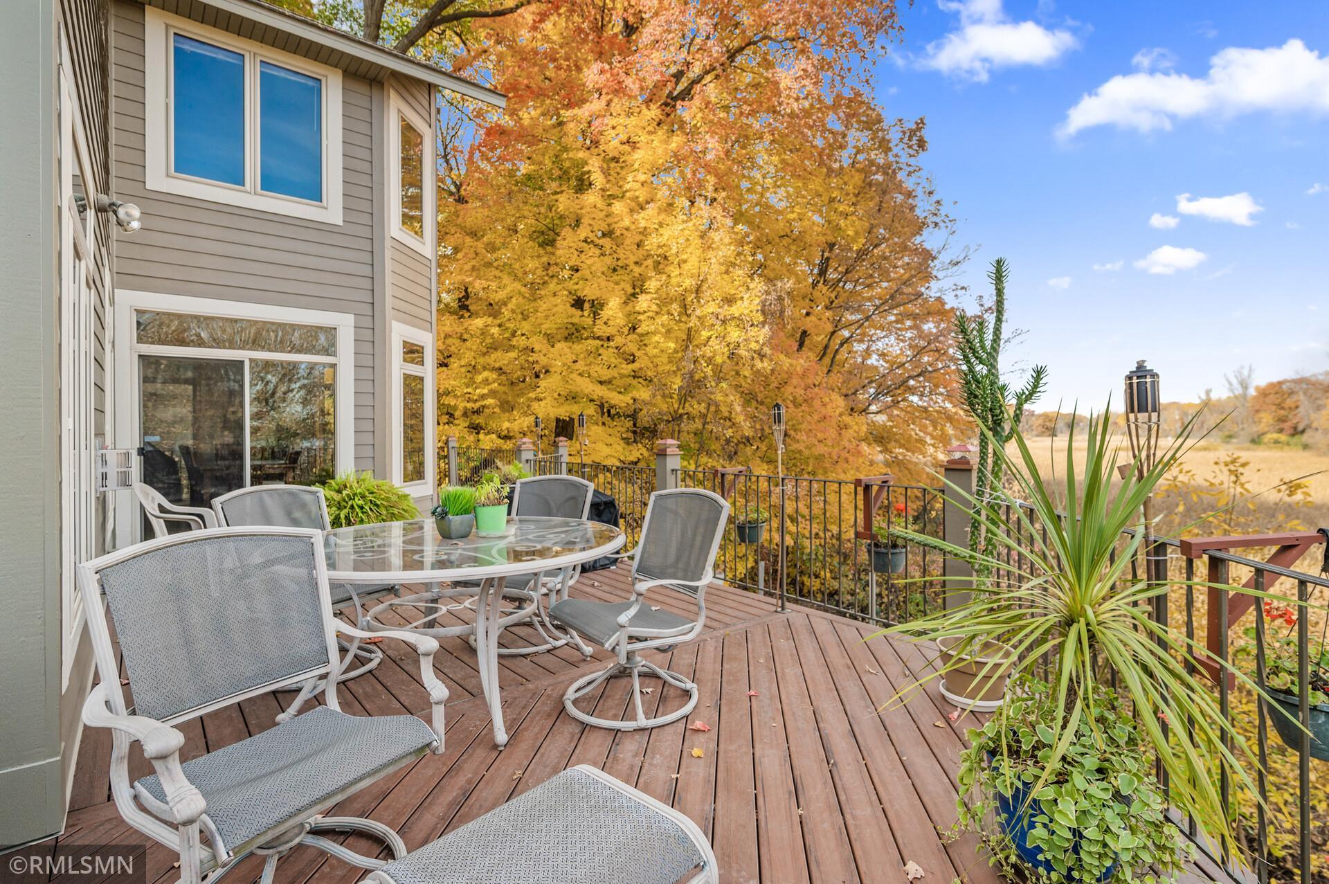 Furnished wooden deck with patio seating overlooking golden autumn trees and an open field.