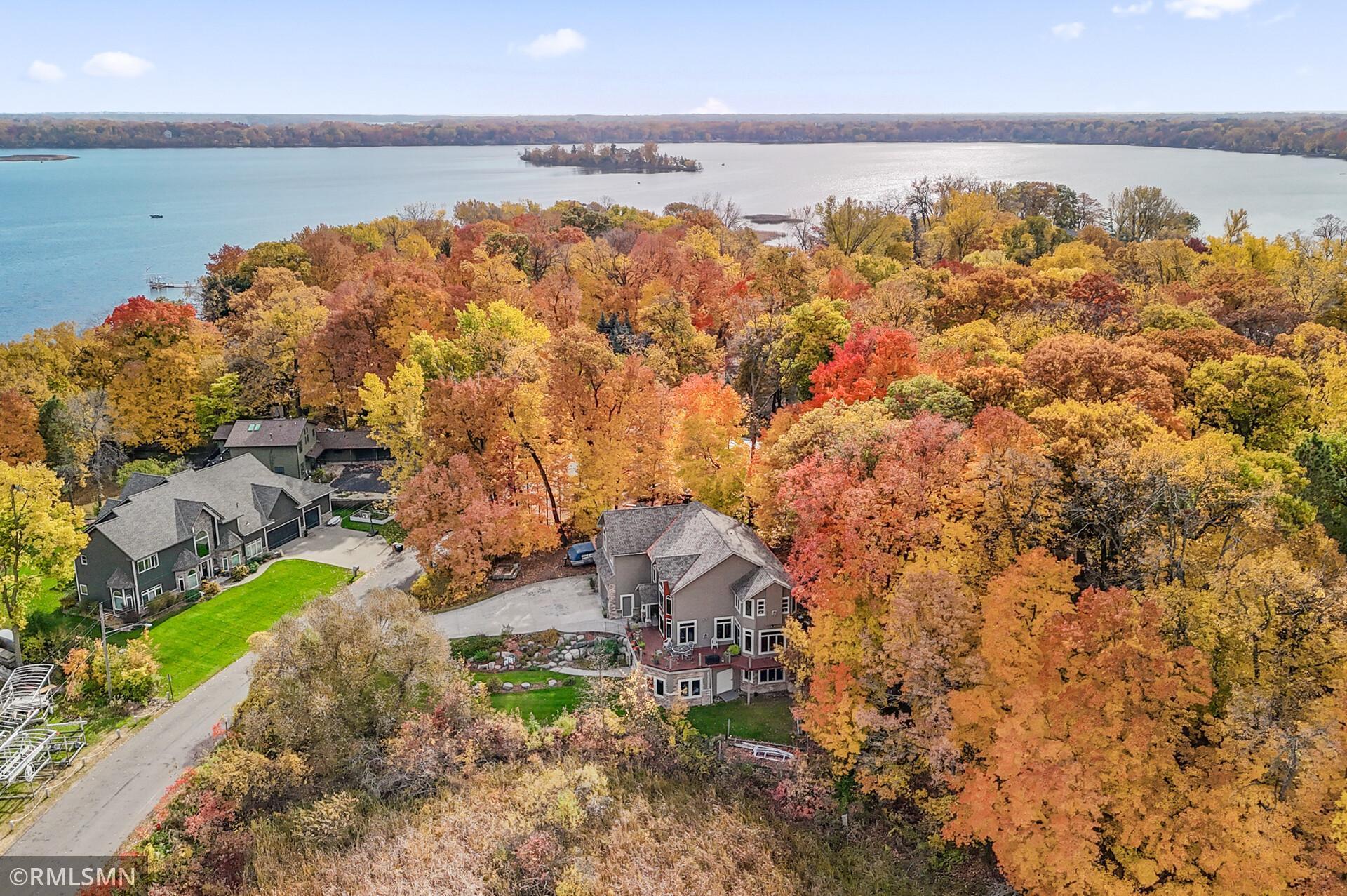 Aerial view of homes among autumn trees beside a lake and small island.