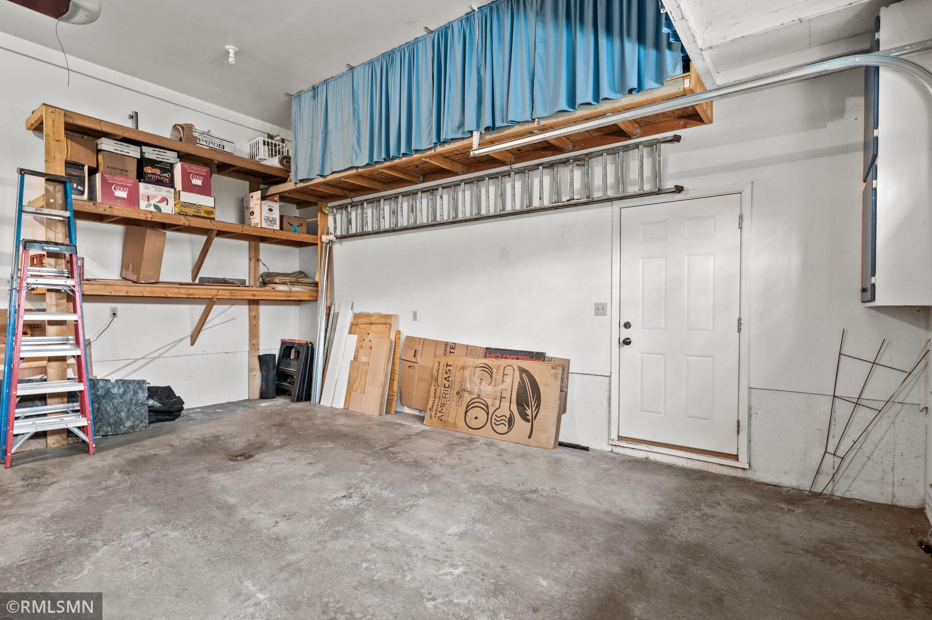 Garage with overhead ladder, wooden storage shelves, boxes, and a white door
