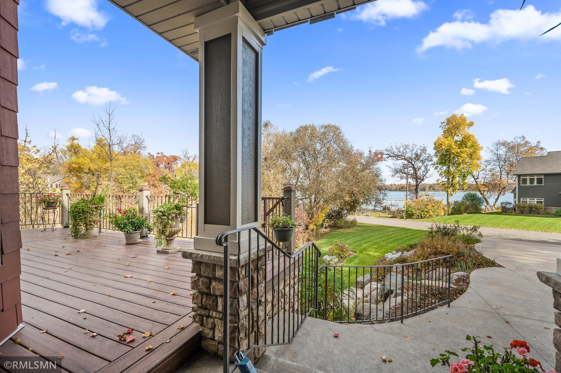 Covered deck overlooking a lake, with potted plants and autumn trees.