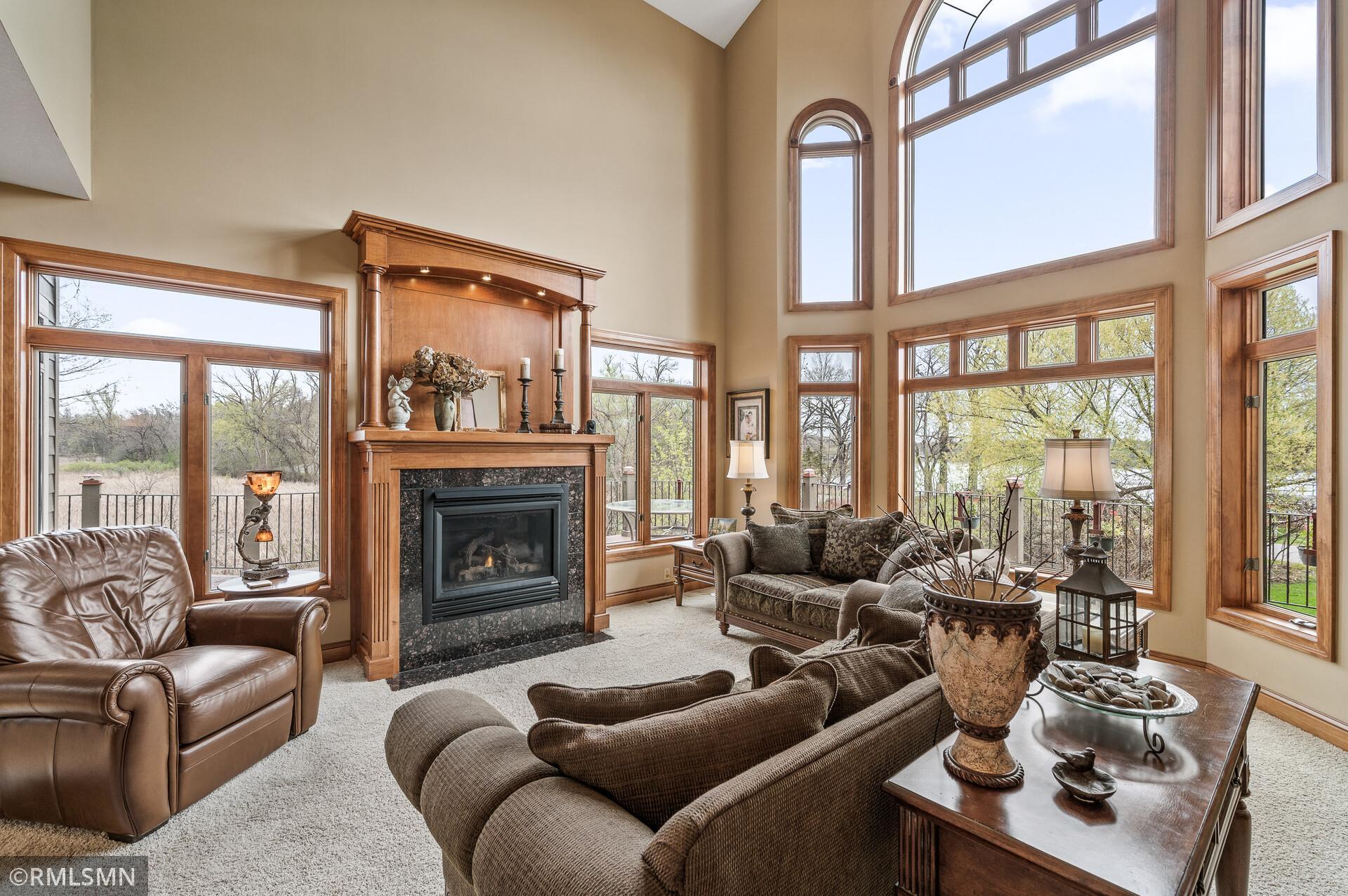 Living room with a wood-mantel fireplace, vaulted ceiling, and large windows overlooking water.