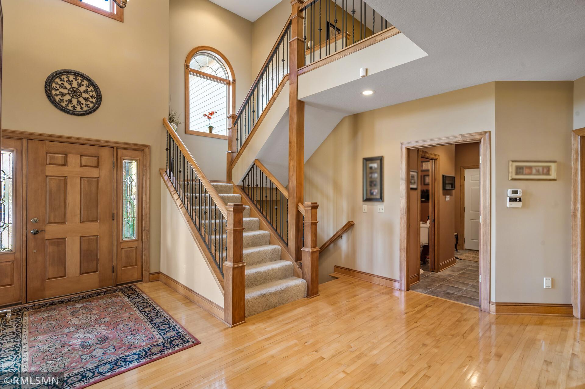 Foyer with a sweeping carpeted staircase, wood railings, arched window, and hardwood floors.