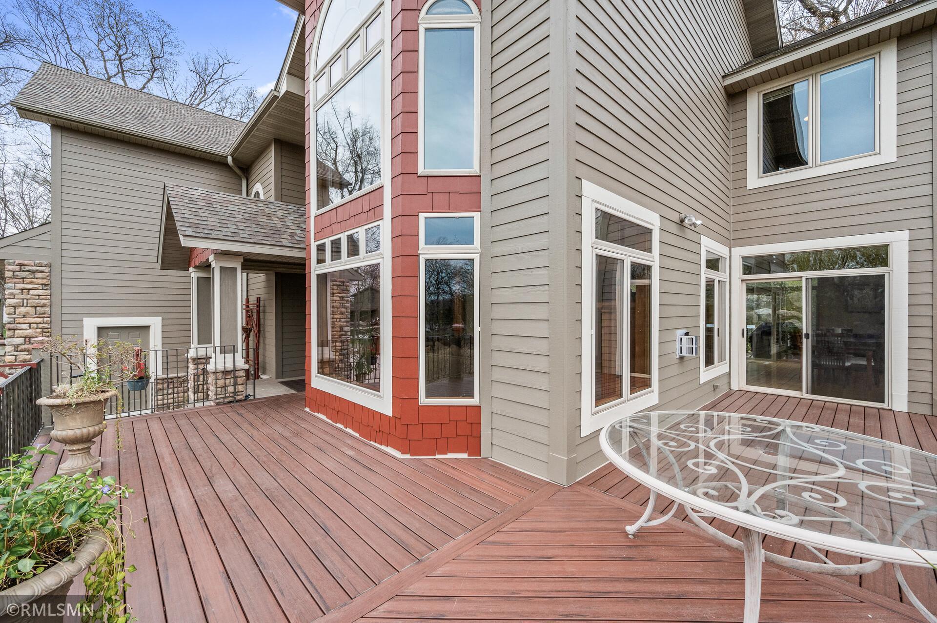 Wraparound wood deck with a glass-top patio table beside a gray and red-sided home.
