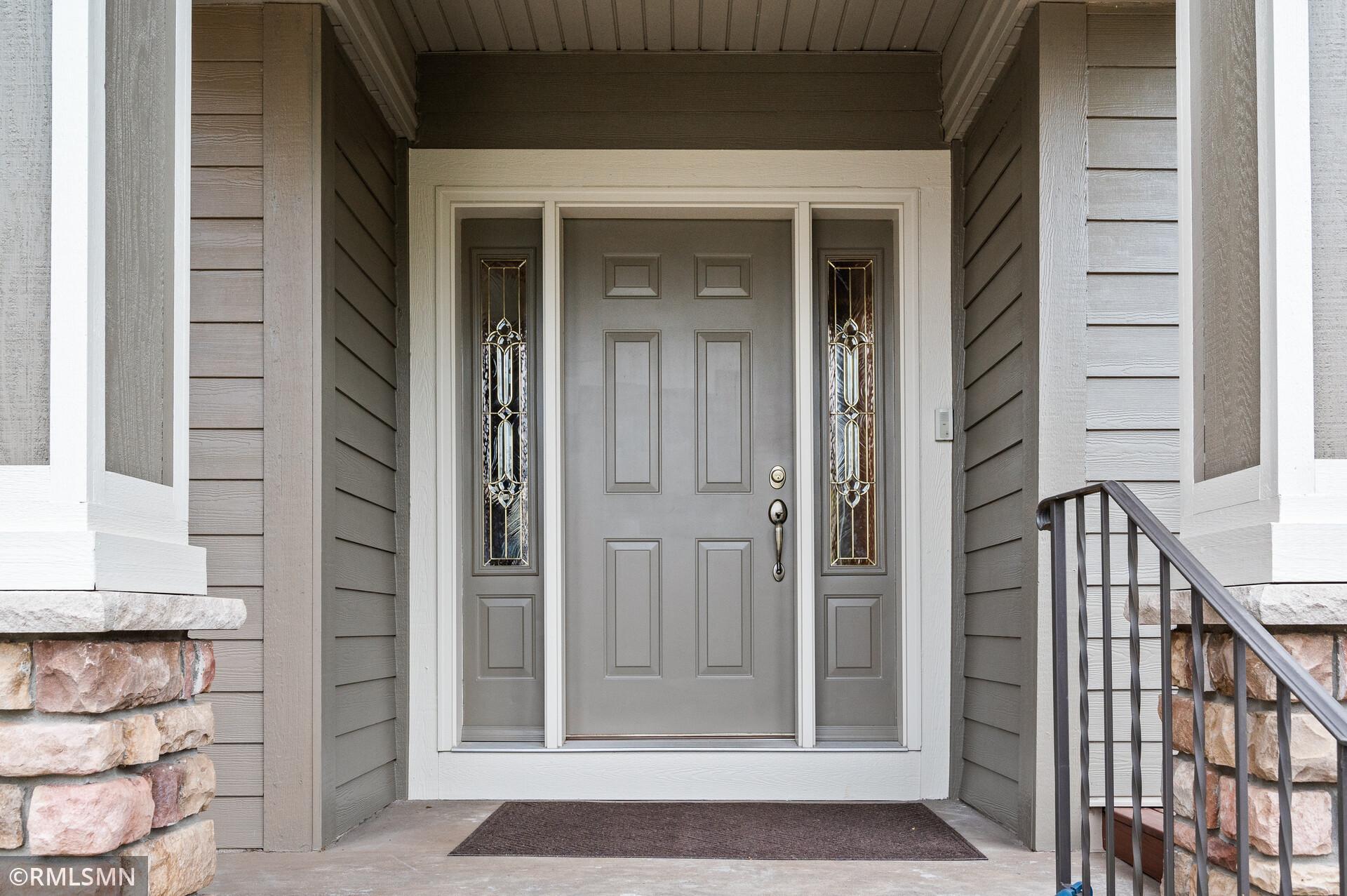 Covered home entry with a gray paneled door, decorative glass sidelights, and stone porch accents.