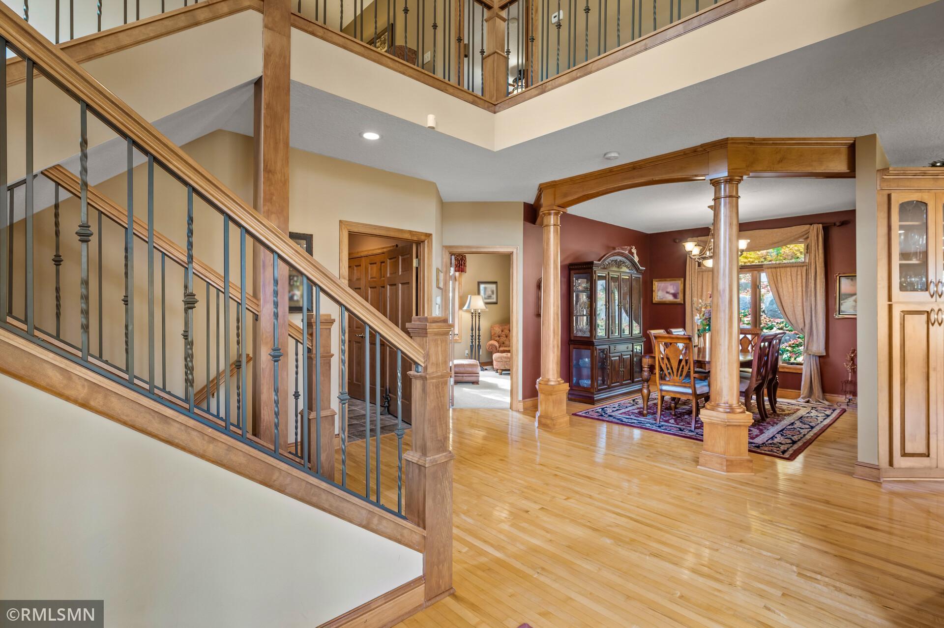 Two-story foyer with a sweeping wood staircase, polished floors, and an arched opening to the dining room.