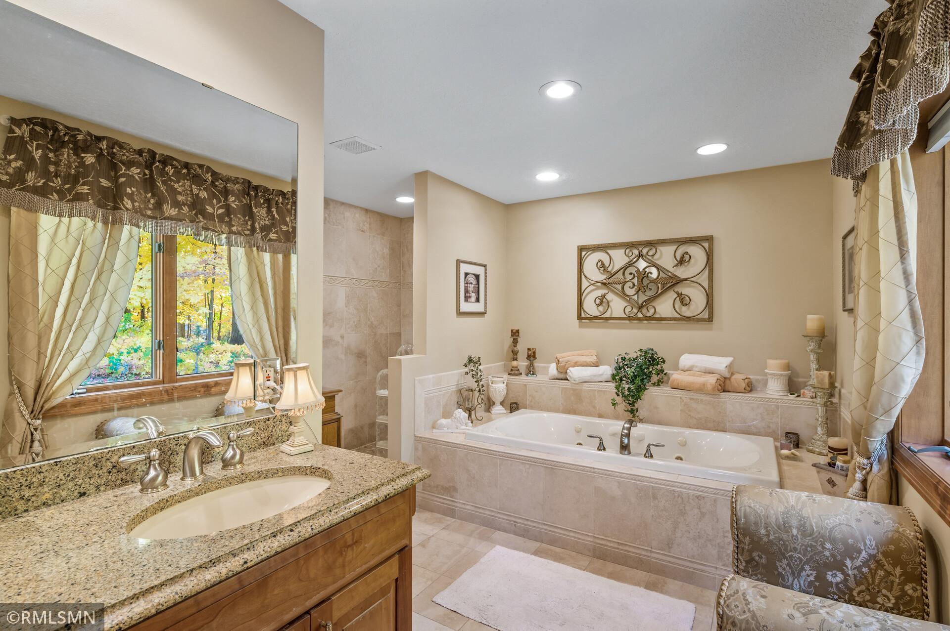 Bathroom with a jetted soaking tub and granite double-sink vanity beside curtained windows.
