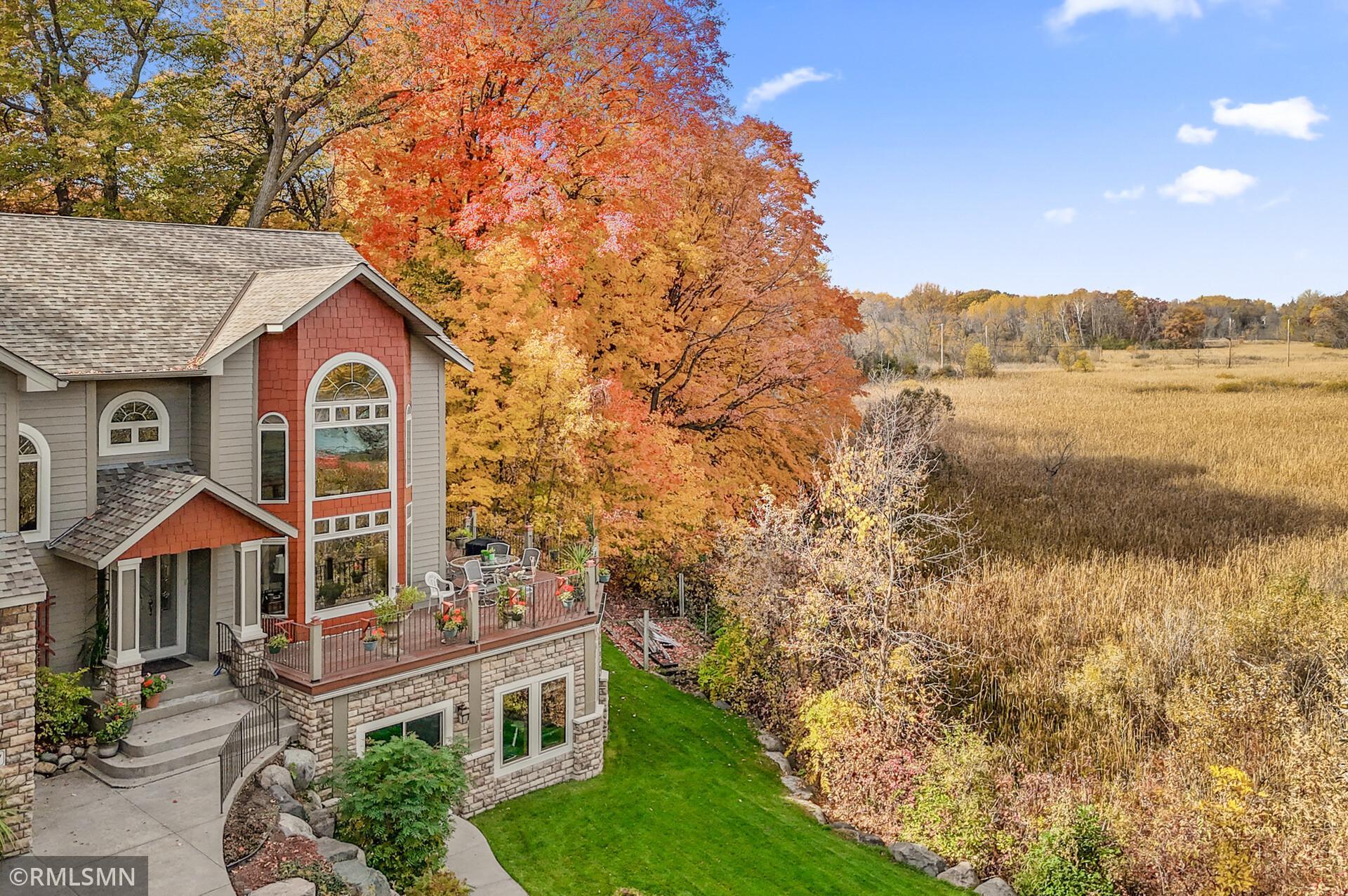 House with a furnished deck beside an open field and colorful autumn trees.
