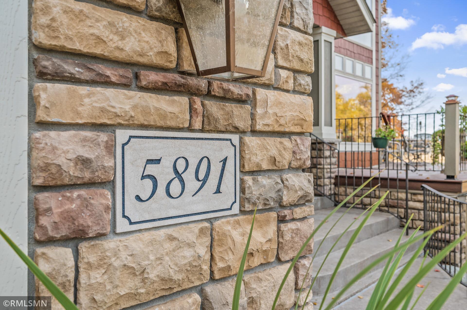 Stone-clad home entrance with 5891 address plaque, lantern, and black metal railings.
