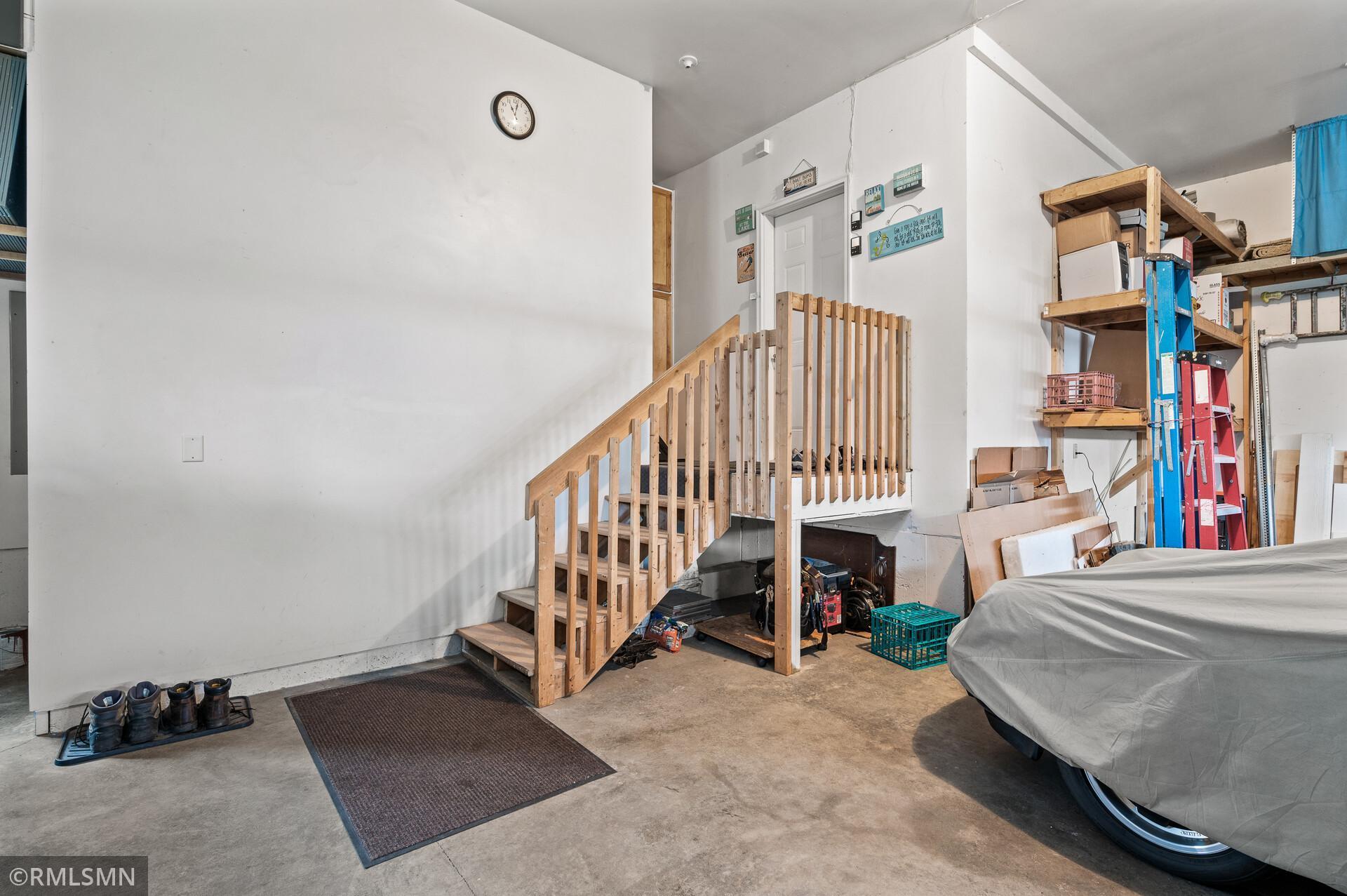 Garage with wooden stairs, storage shelving, and a covered vehicle.