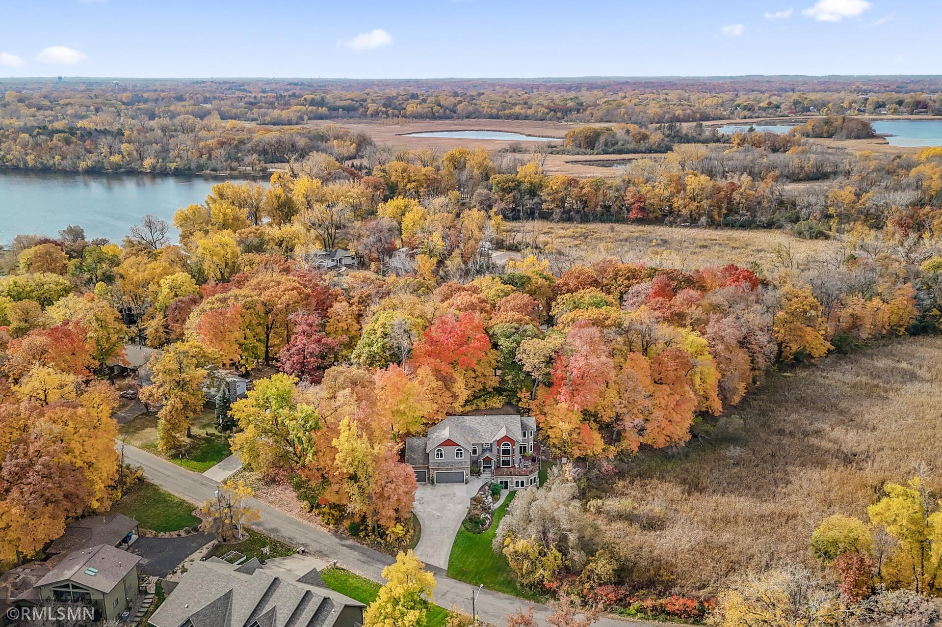 Aerial view of a home amid autumn trees beside wetlands and water.