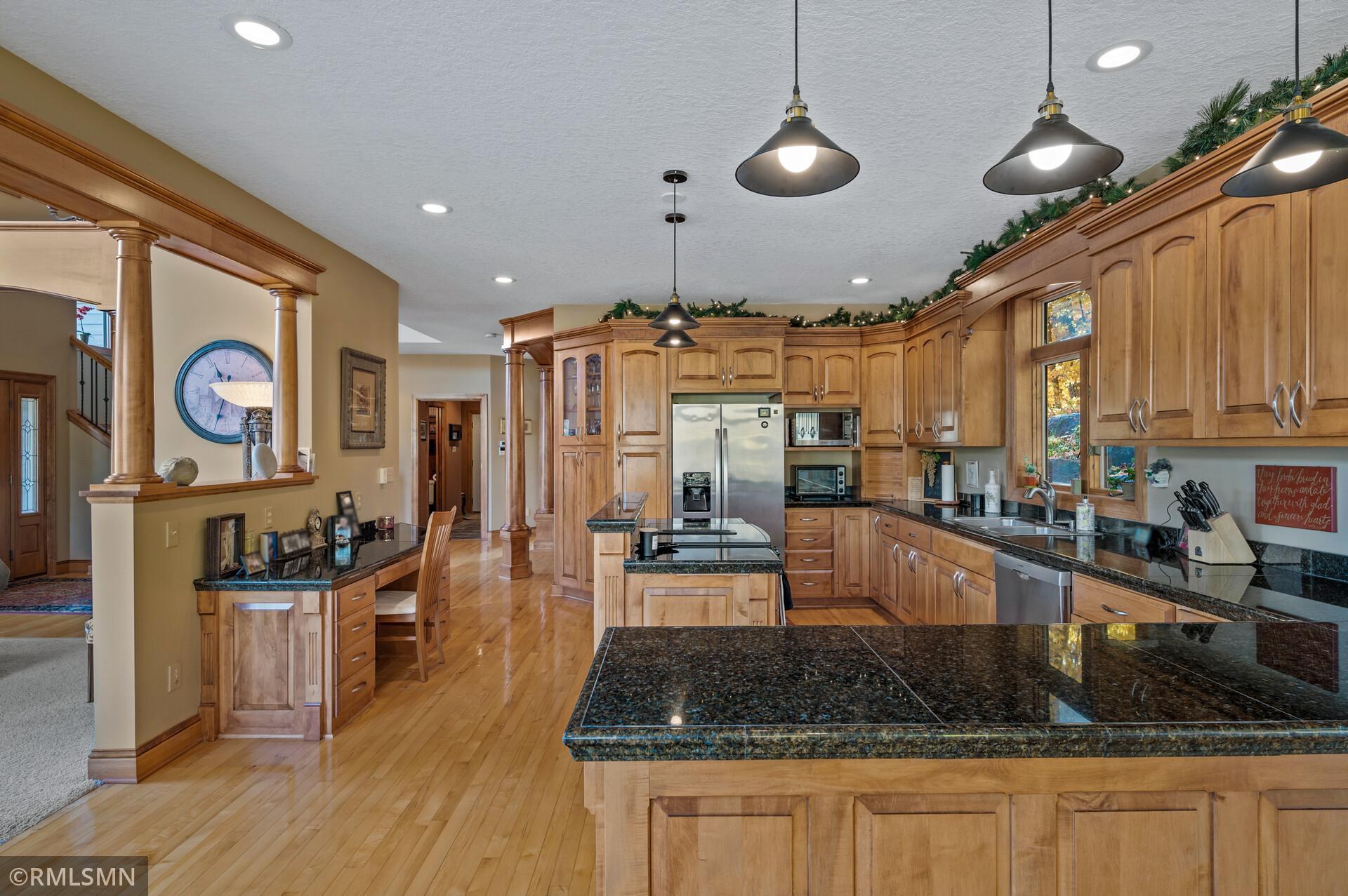Spacious kitchen with wood cabinetry, granite island, stainless steel appliances, and hardwood floors.