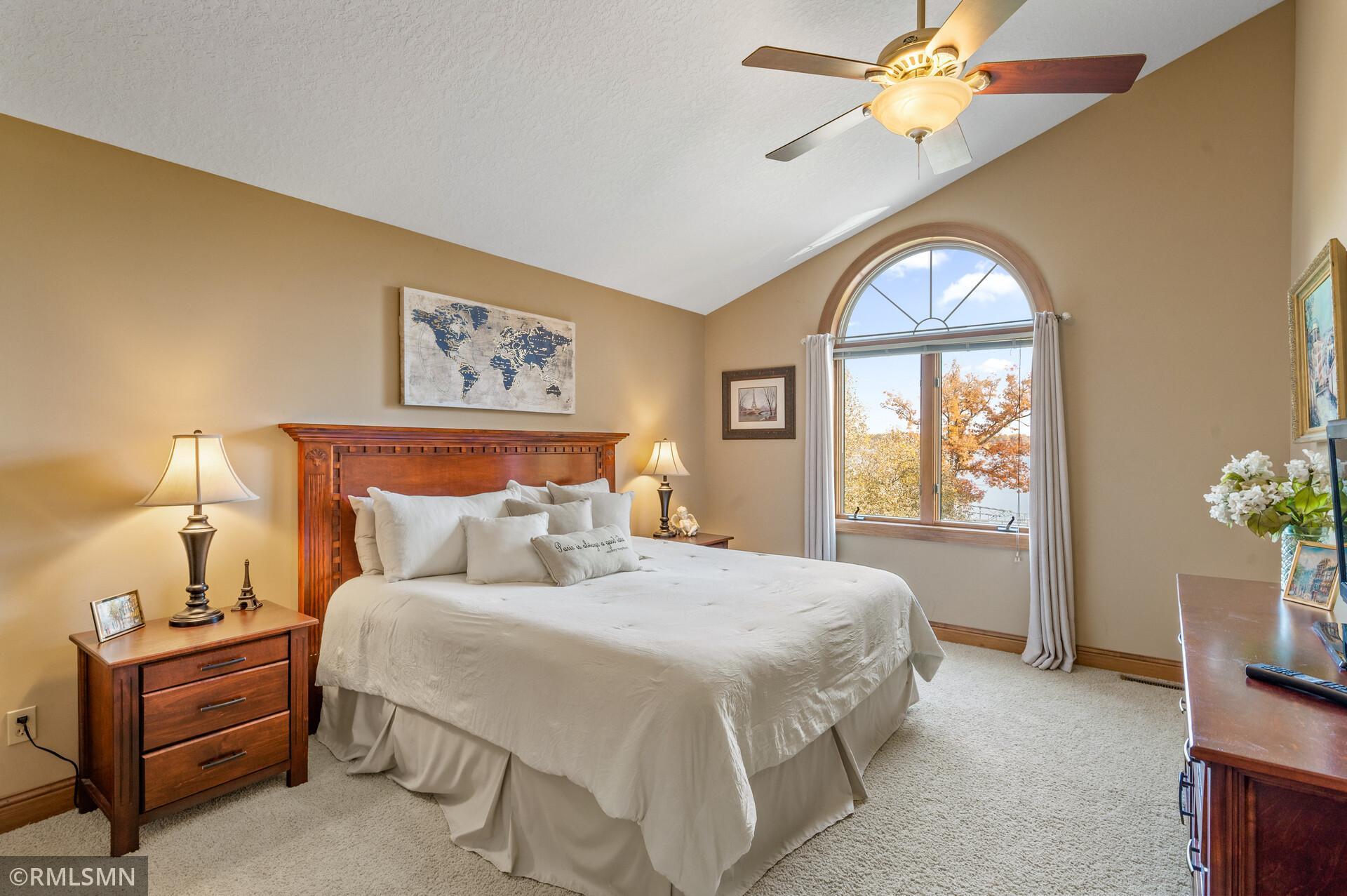 Bedroom with a large wooden bed and an arched window overlooking autumn trees.