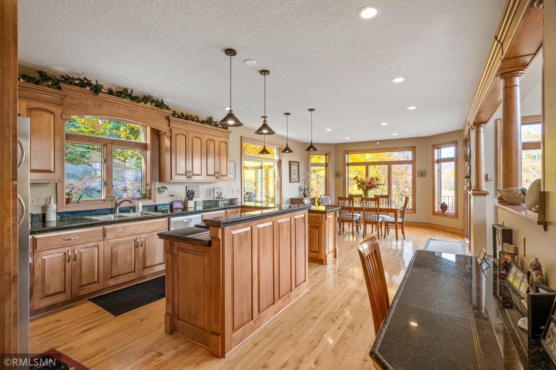 Kitchen with extensive wood cabinetry, a large island, dark stone counters, and an adjoining window-lit dining area.