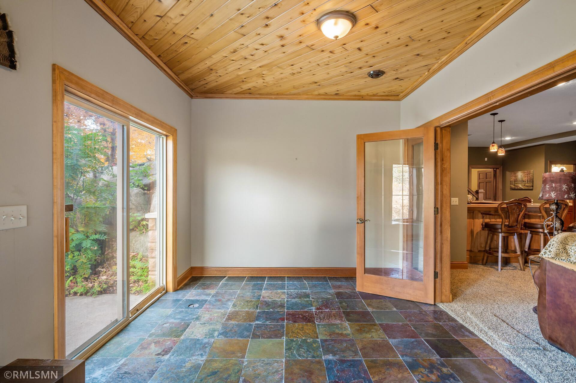 Sunroom with slate tile flooring, a wood-paneled ceiling, and a large glass door overlooking autumn foliage.