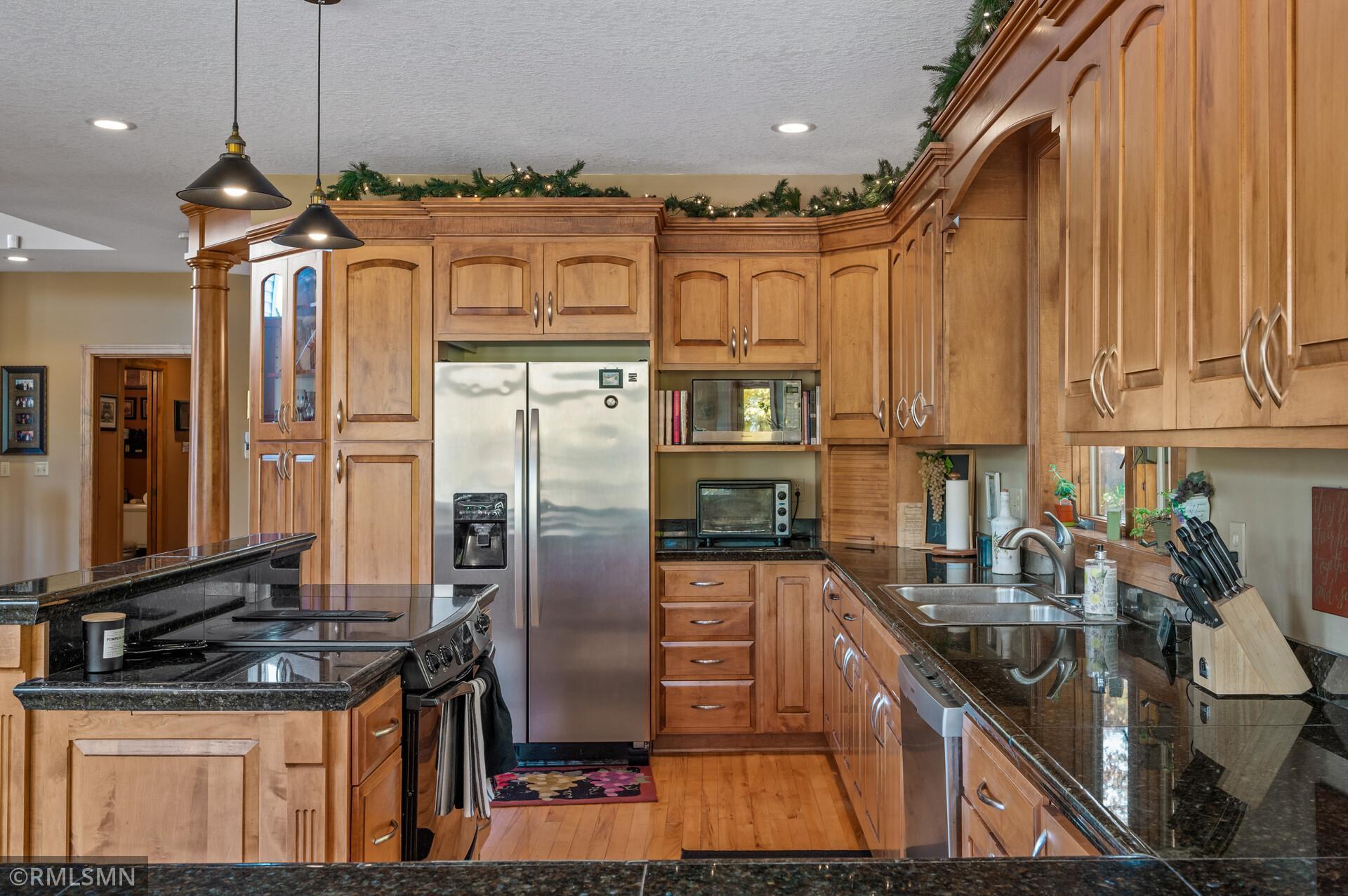 Kitchen with extensive honey-colored cabinetry, black granite counters, stainless steel appliances, and holiday garland.