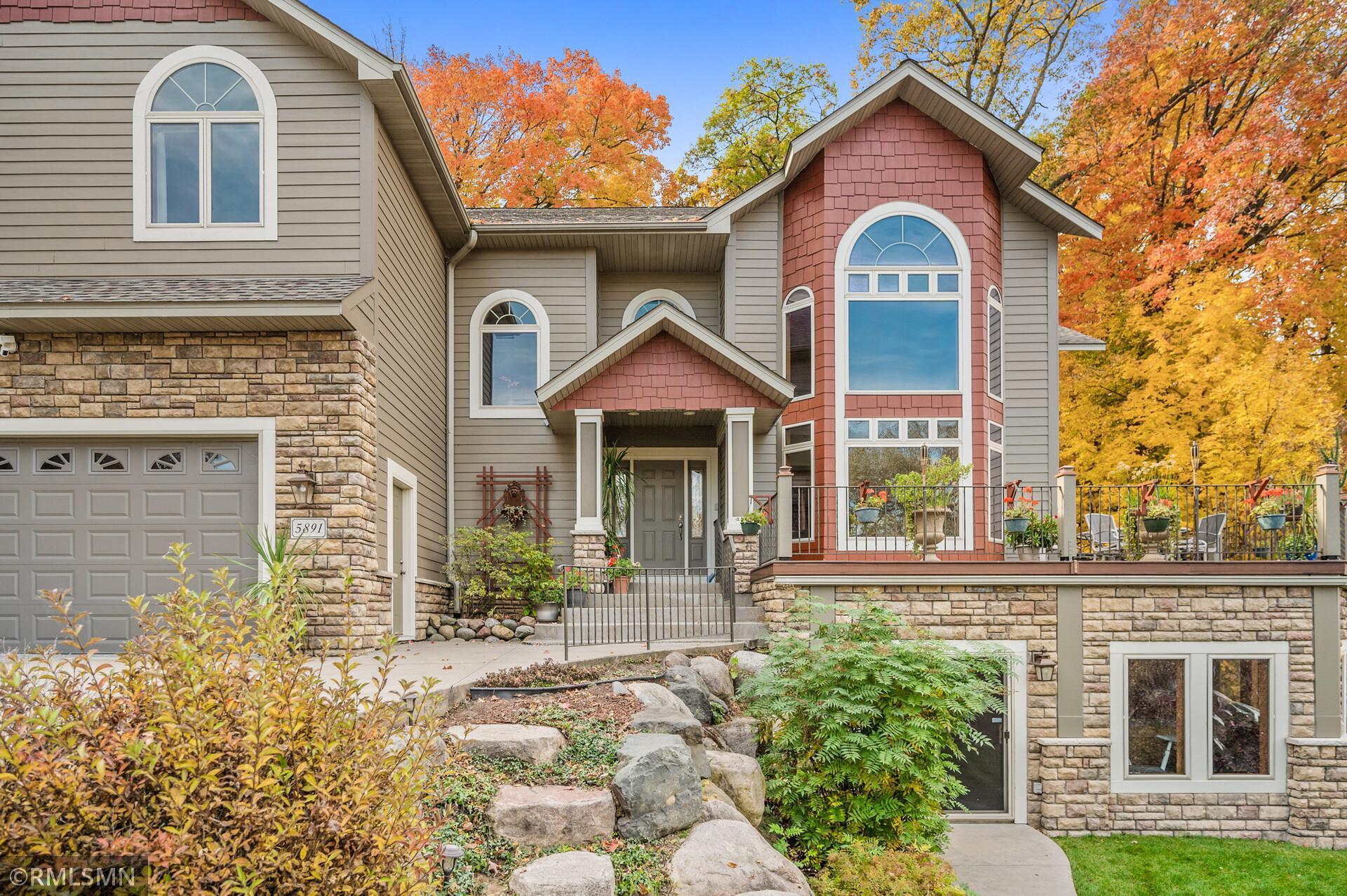 House exterior with stone veneer, red shingle accents, arched windows, and a raised patio deck.
