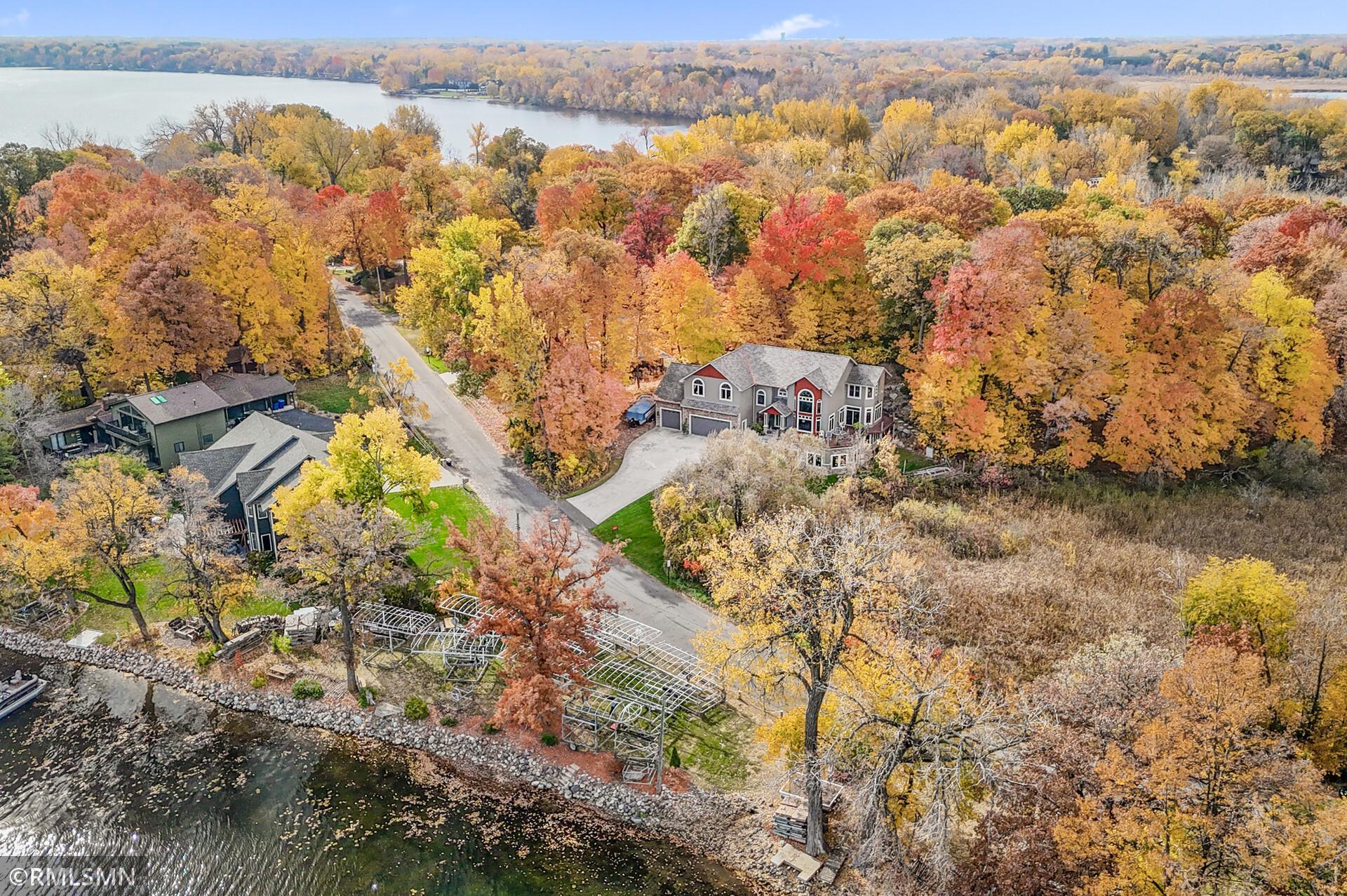 Lakeside two-story home surrounded by colorful autumn trees, seen from above.