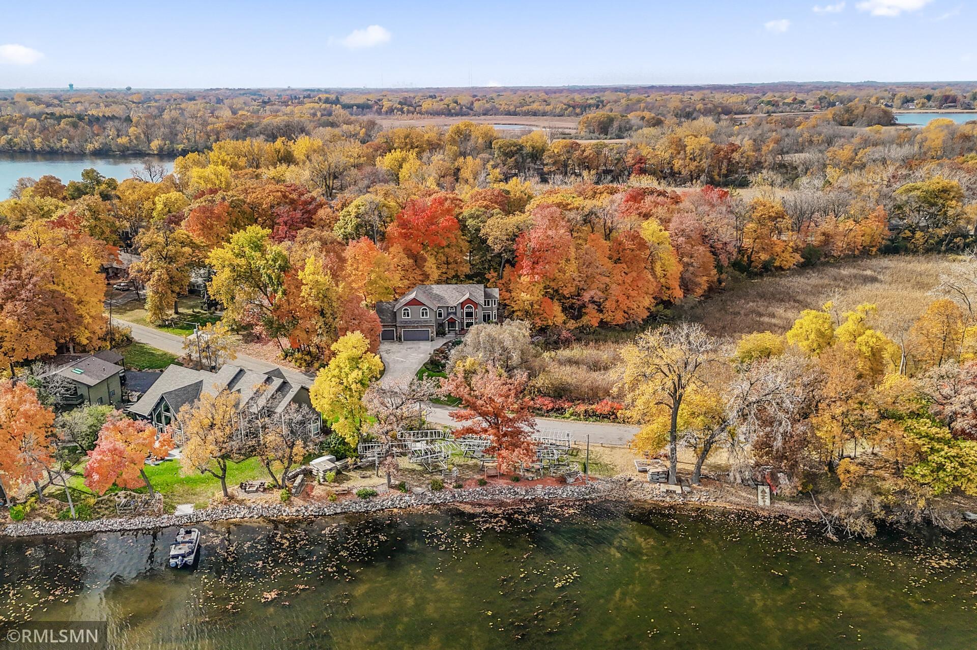 Aerial view of lakeside home amid colorful autumn trees, with a shoreline dock and water.