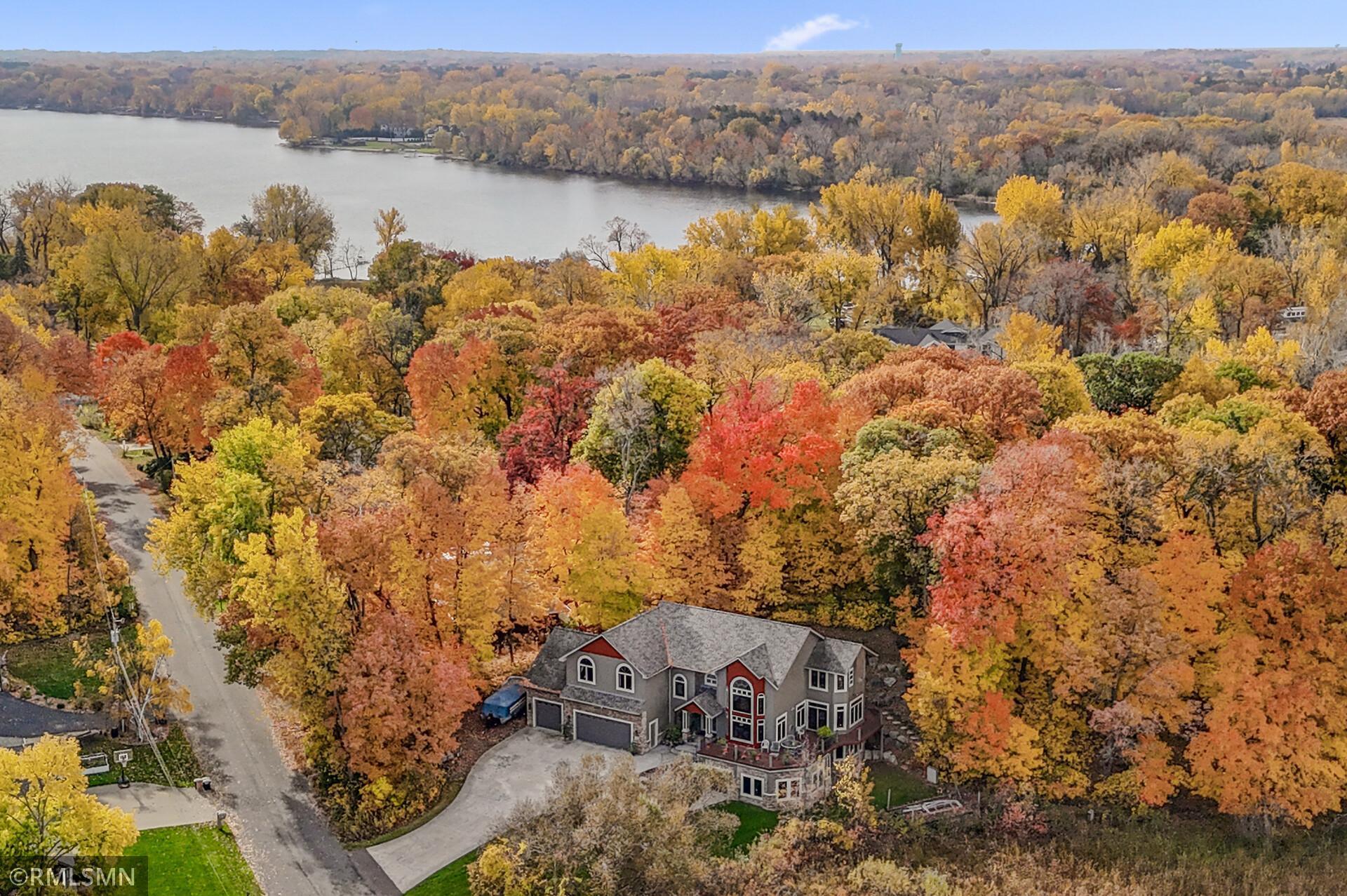 Aerial view of a large gray house amid autumn foliage, with a lake in the background.