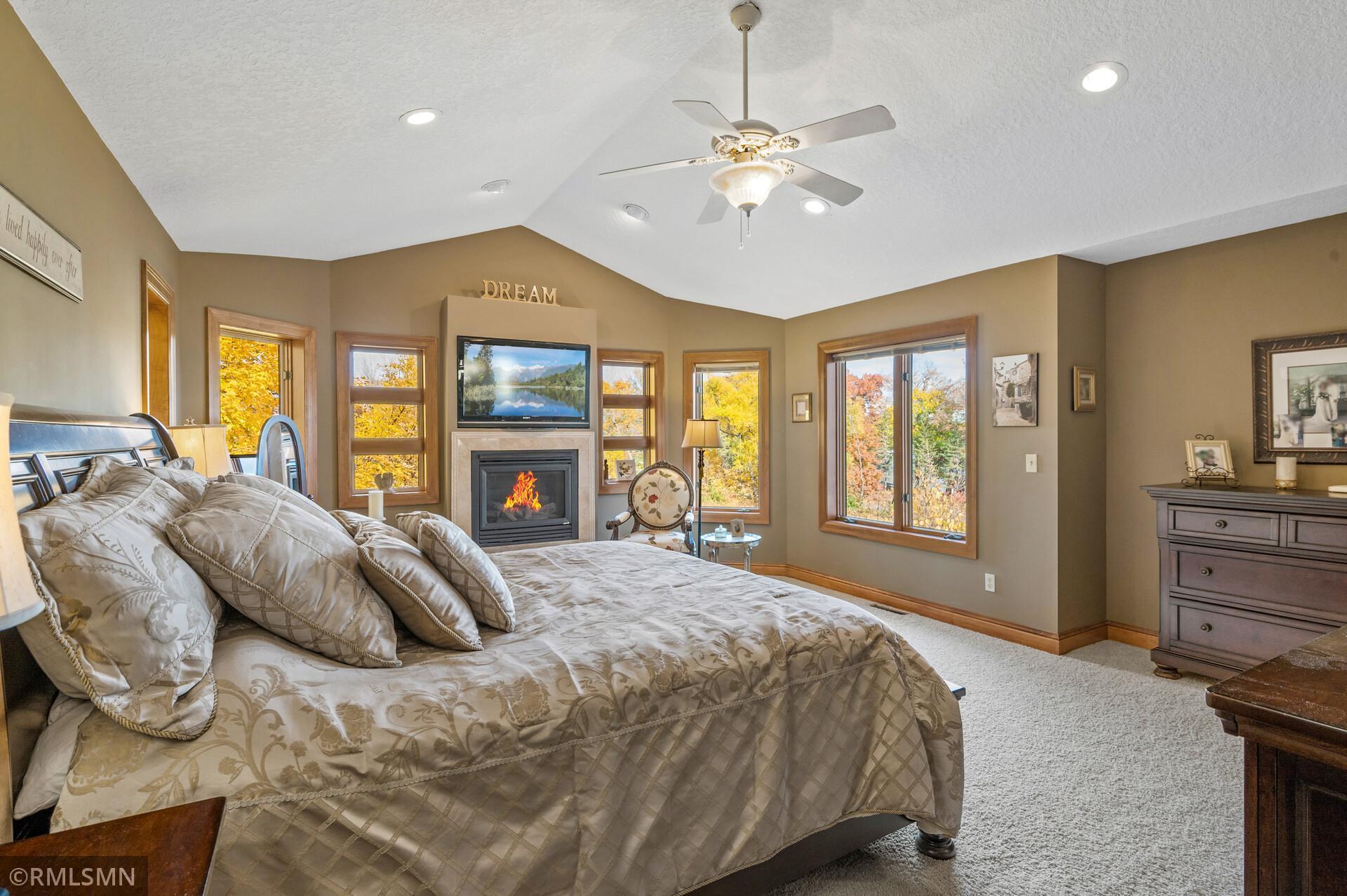 Furnished bedroom with a fireplace, large bed, and windows overlooking autumn foliage.