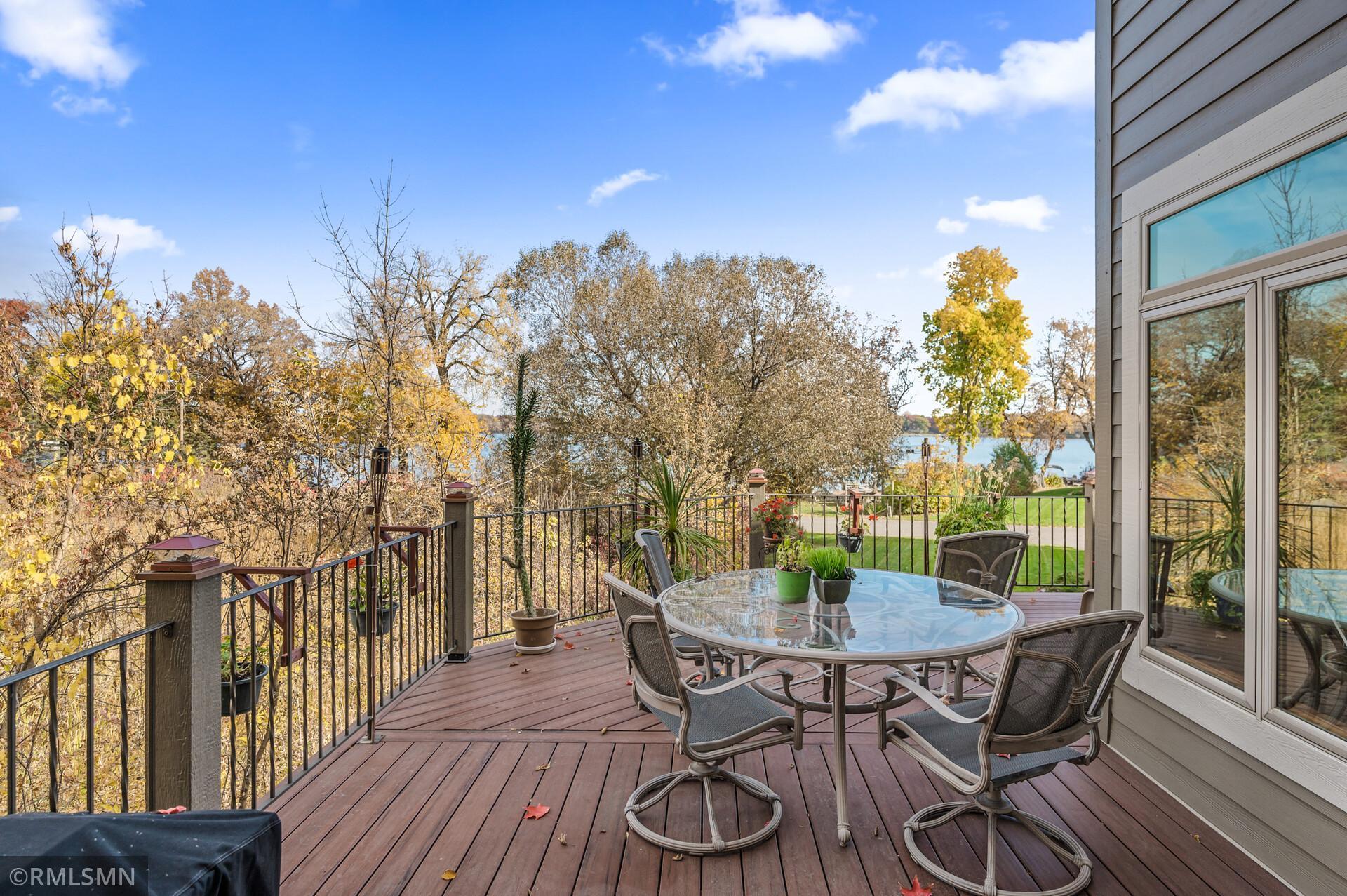 Furnished deck with a glass patio table and chairs overlooking autumn trees and a lake.