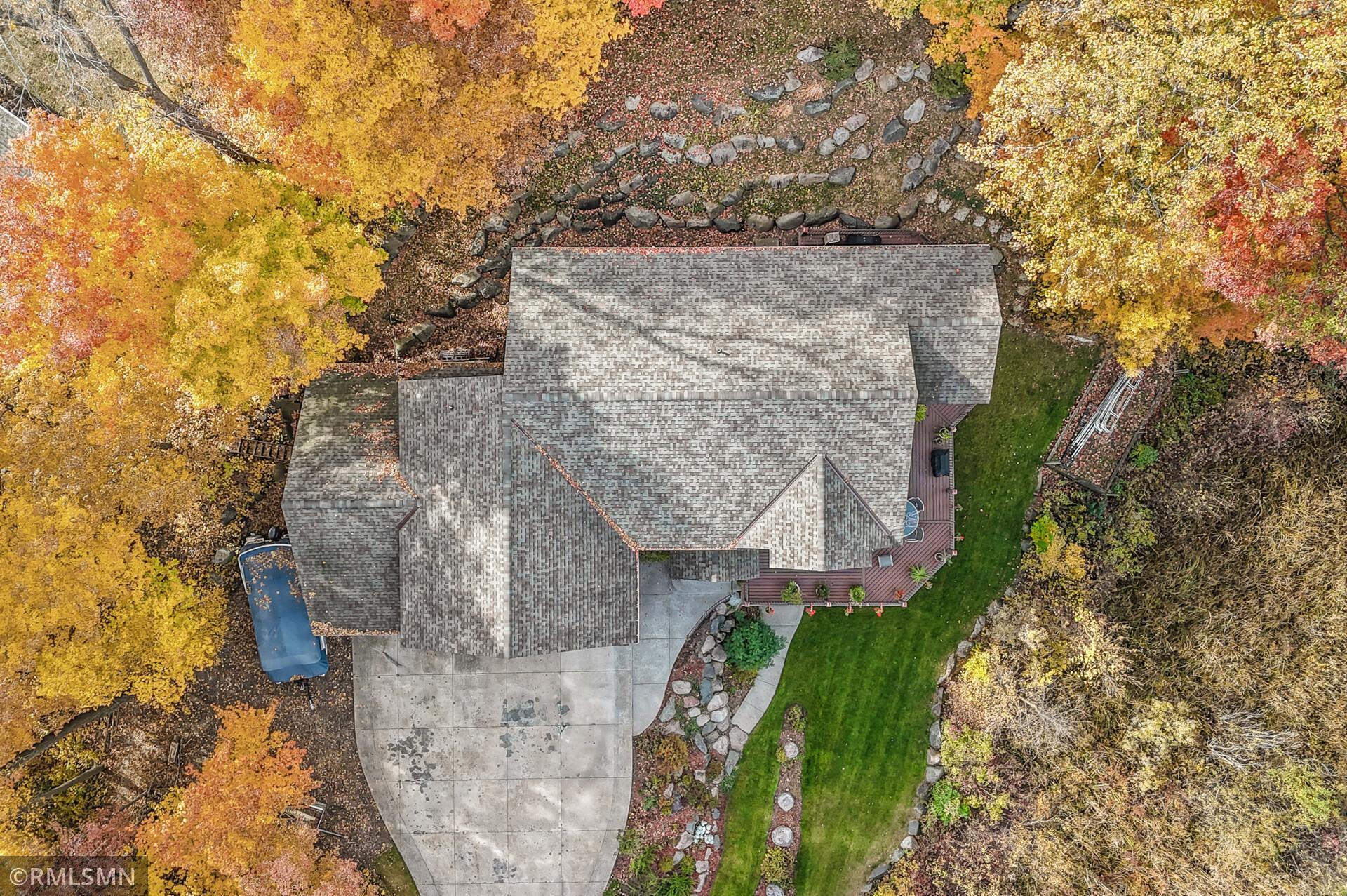 Aerial view of a home, deck, driveway, and landscaped yard amid colorful autumn trees.