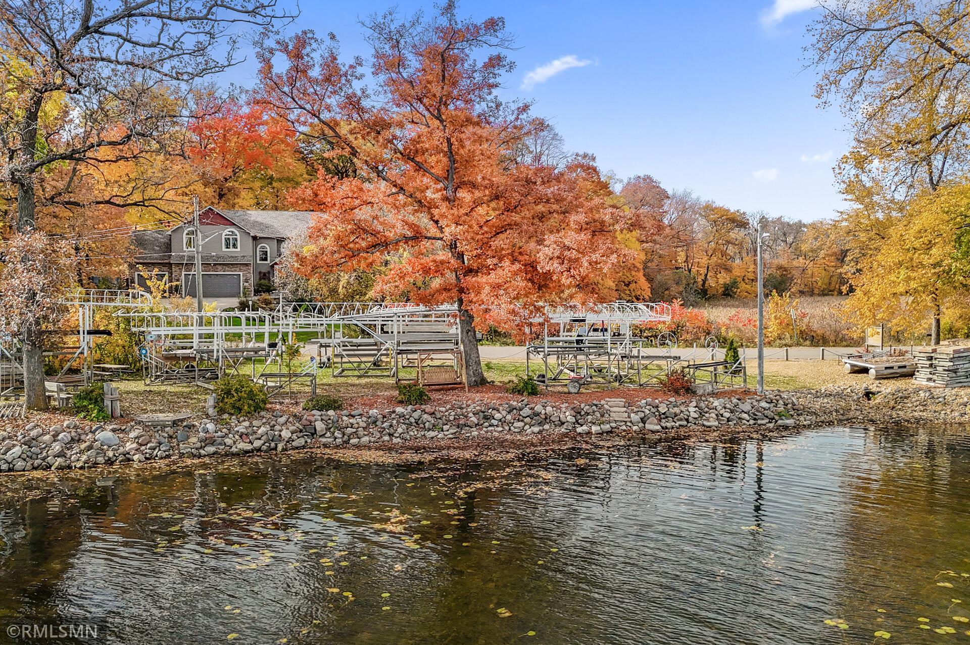 Waterfront house and docks across the water, framed by colorful autumn trees.