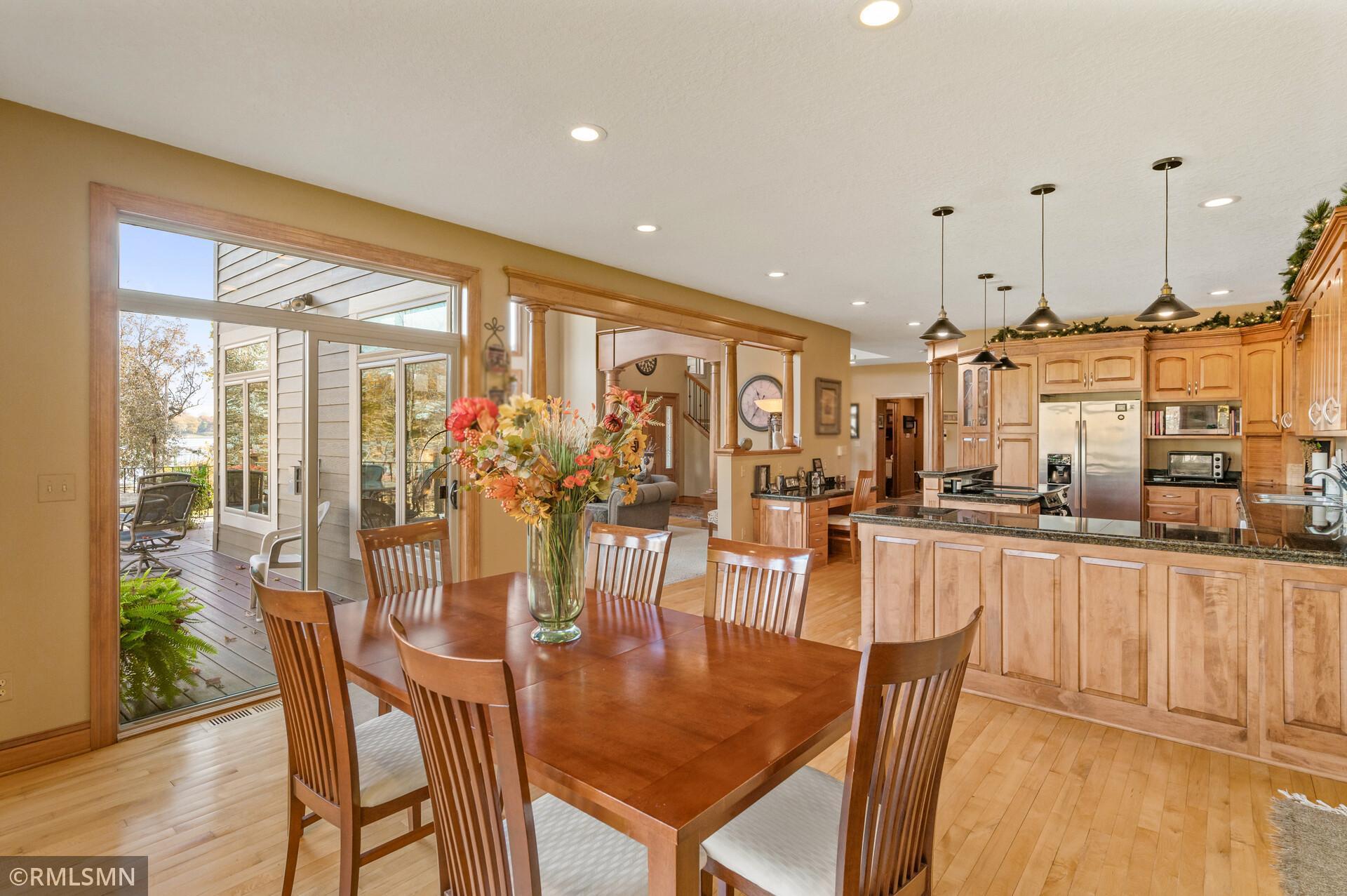 Dining table beside a wood-cabinet kitchen, with a deck and water visible through the windows.