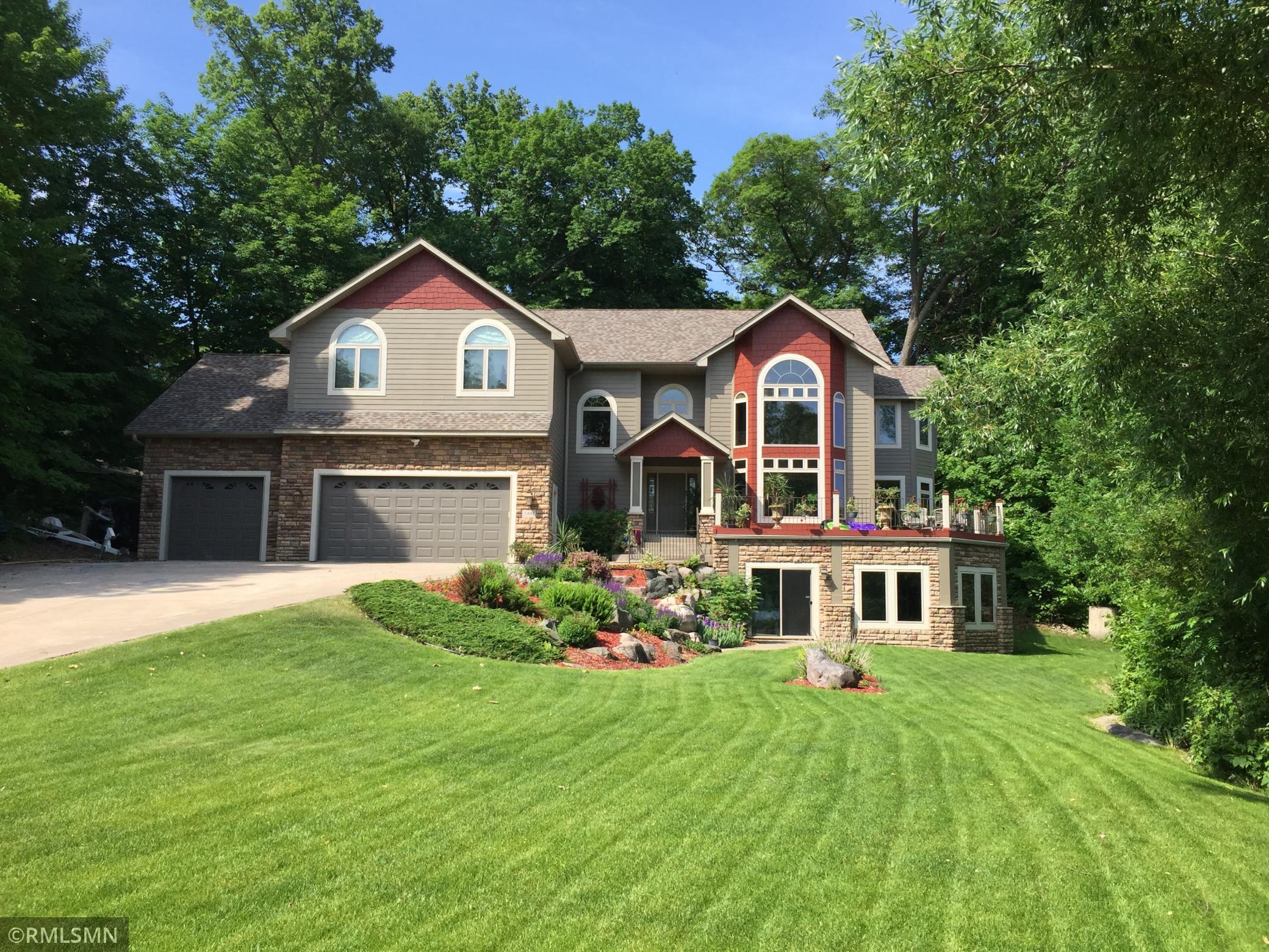 Two-story home with stone and siding, a three-car garage, arched windows, and a landscaped lawn.
