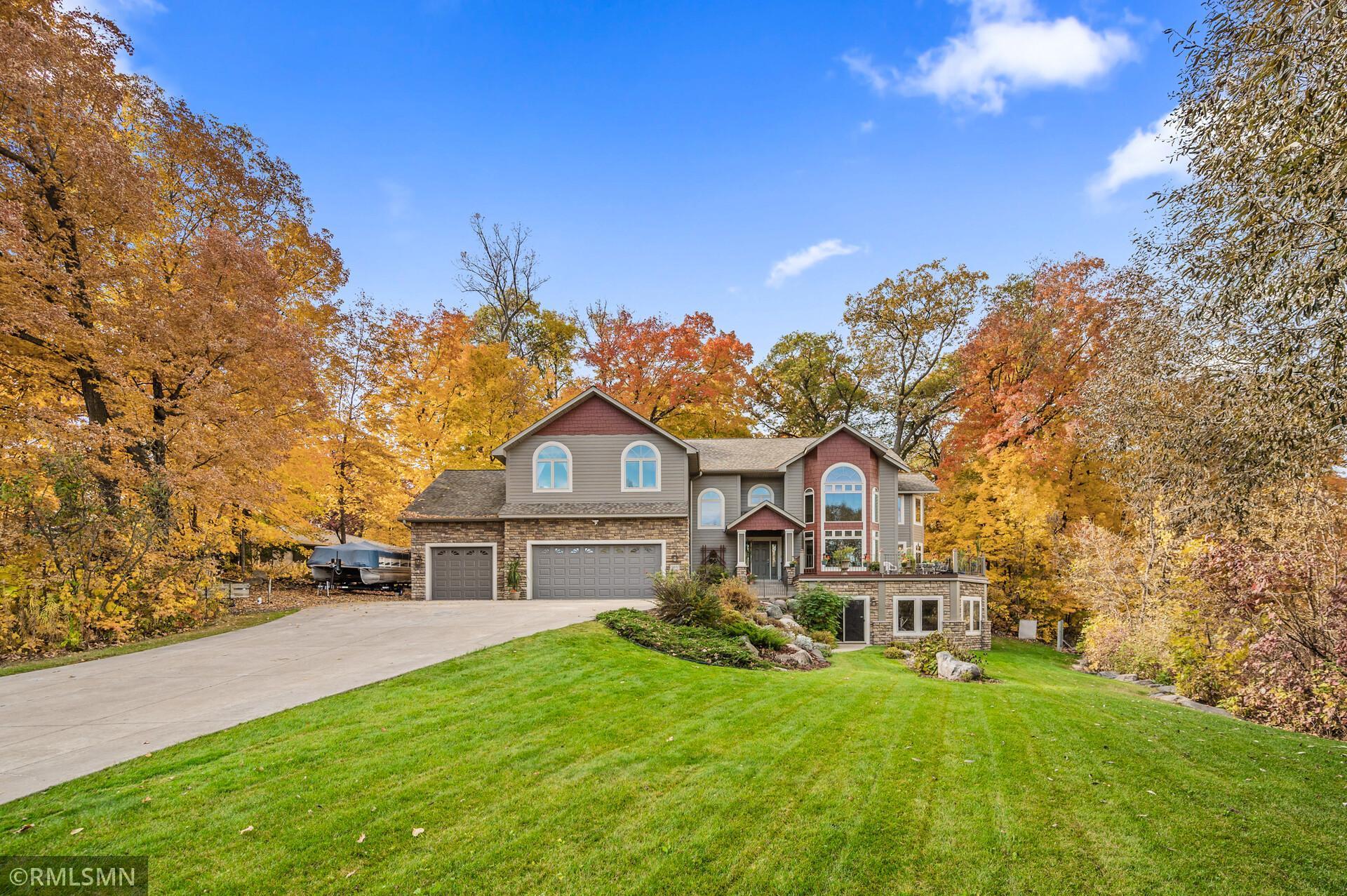 Two-story gray and stone home with a three-car garage, broad driveway, and autumn trees.