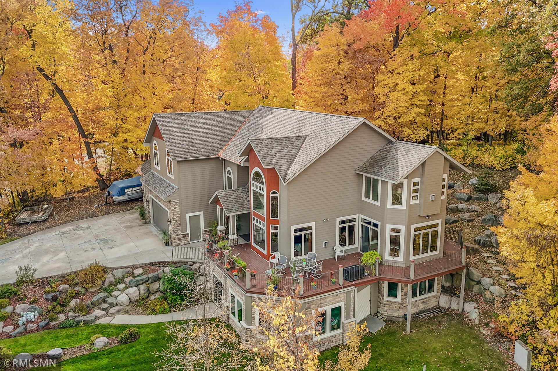 Aerial view of a multi-level home with a wraparound deck amid colorful autumn trees.