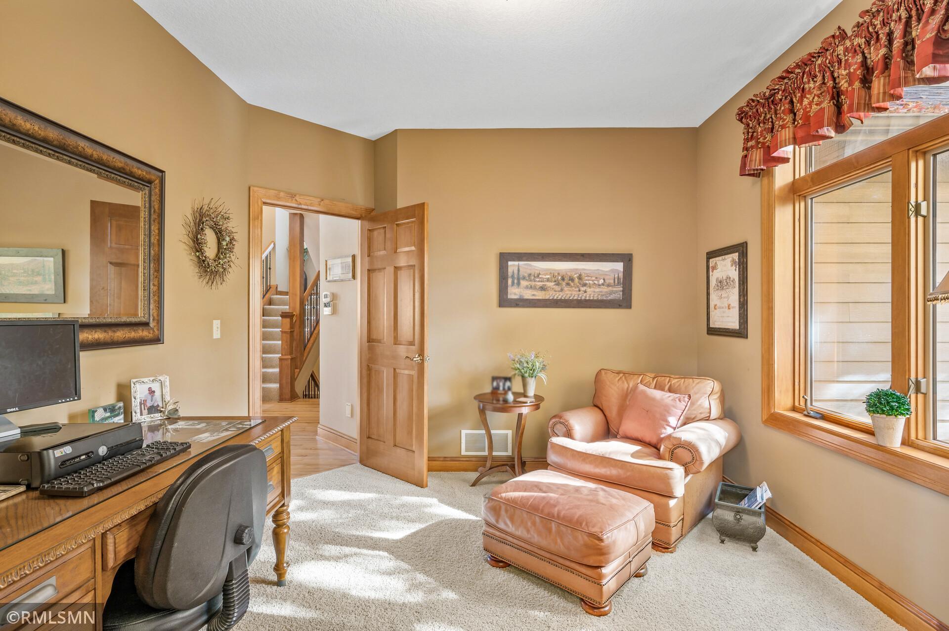 Furnished home office with a carved desk, tan leather armchair and ottoman, and a sunlit window.