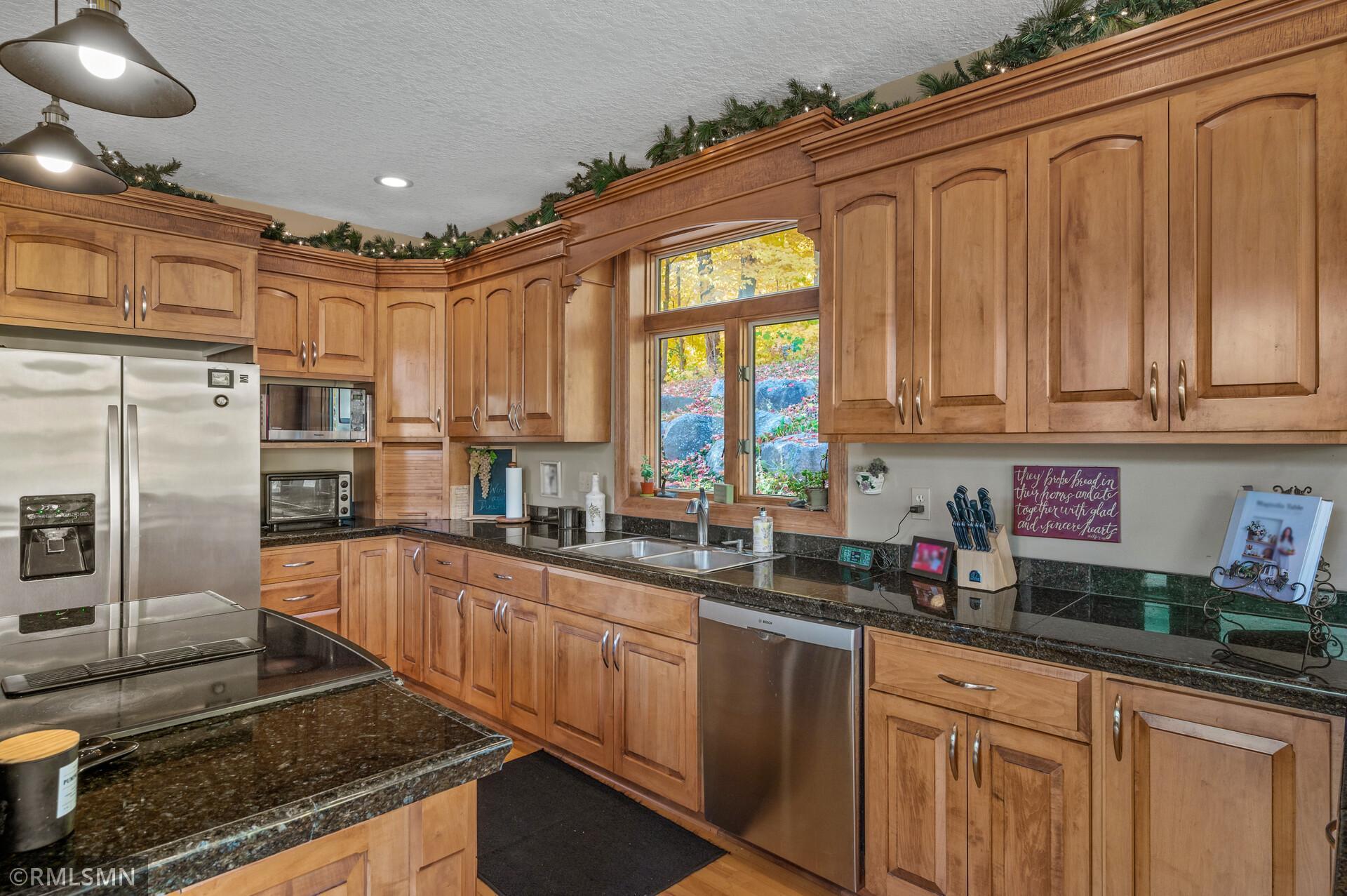 Kitchen with extensive honey-colored wood cabinetry, granite counters, stainless appliances, and an autumn view through the window.