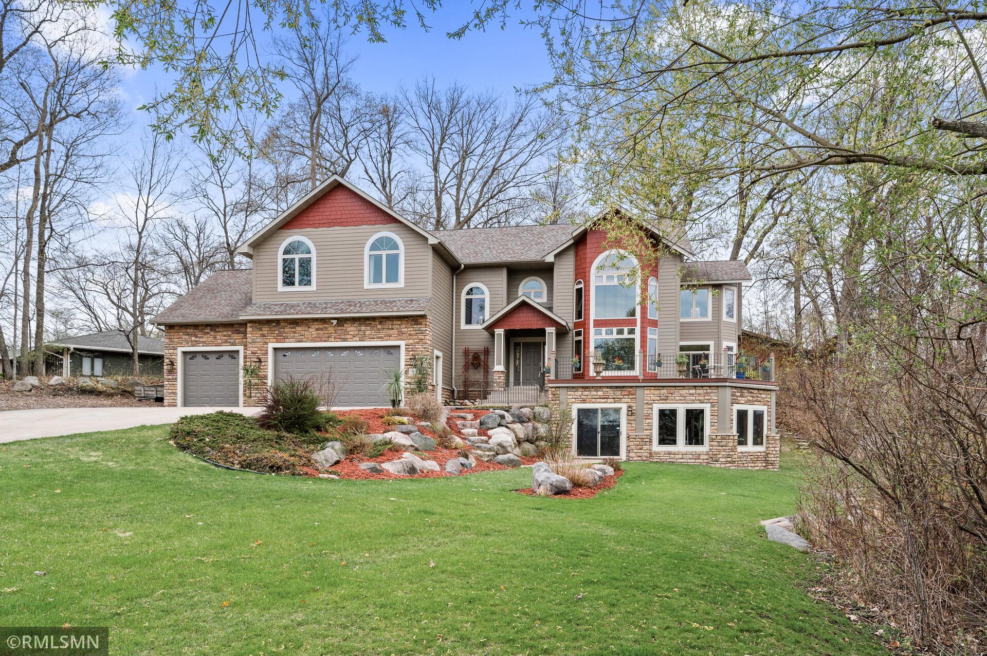 Two-story home with stone accents, a three-car garage, raised deck, and landscaped lawn.