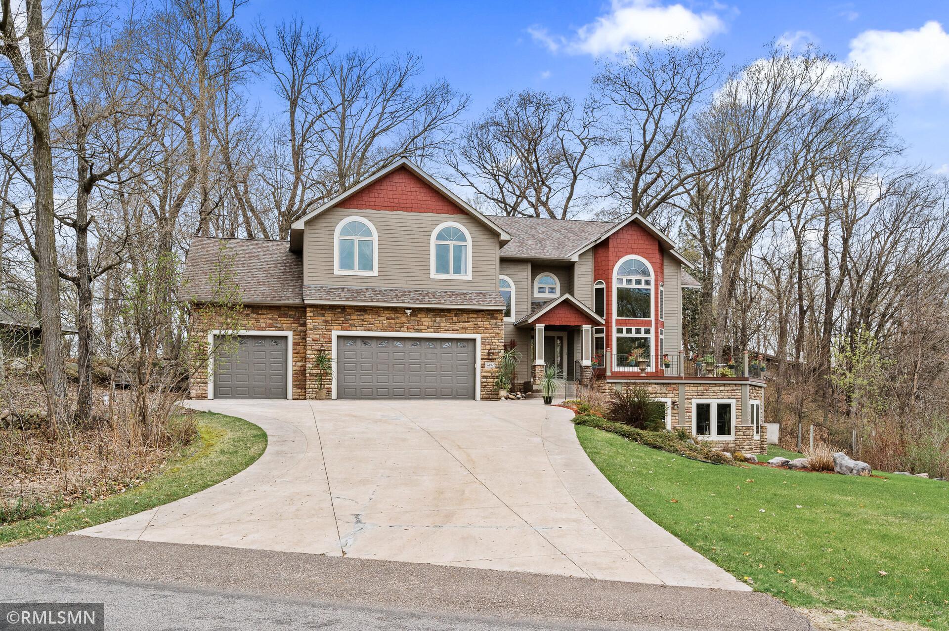 Two-story home with red gables, stone accents, arched windows, and a three-car garage.