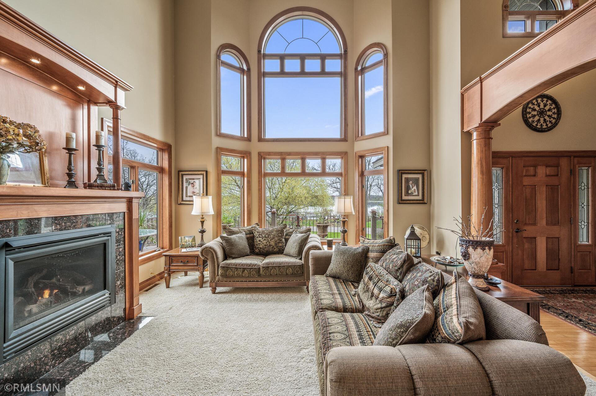 Living room with a stone fireplace, tall arched windows, and lake views.