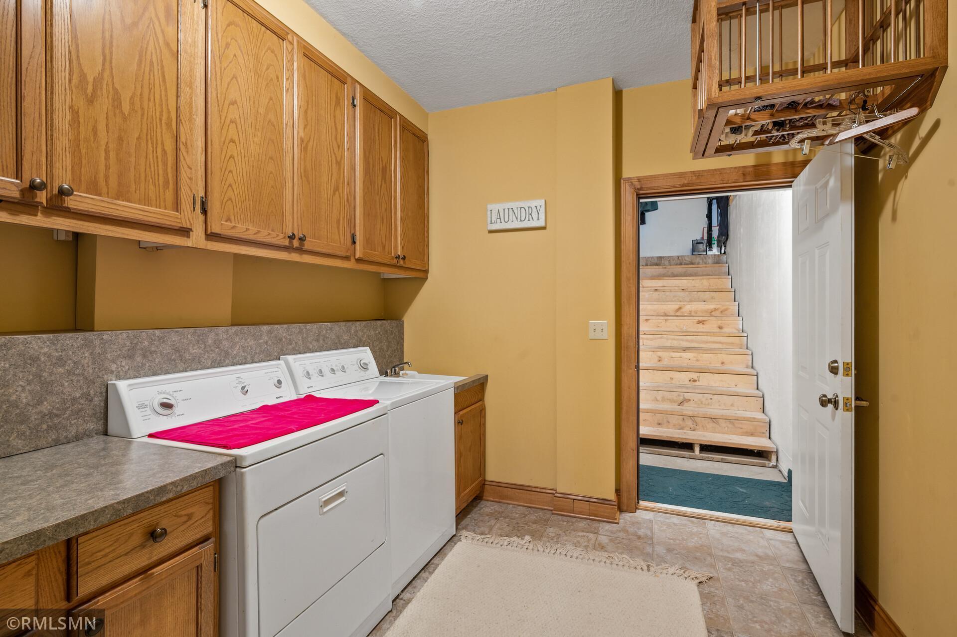 Laundry room with white washer and dryer, oak cabinets, and an open doorway to a wooden staircase.