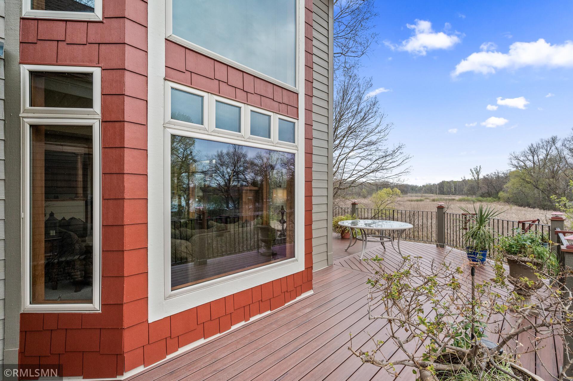 Red-shingled home beside a wood deck overlooking a grassy wetland.